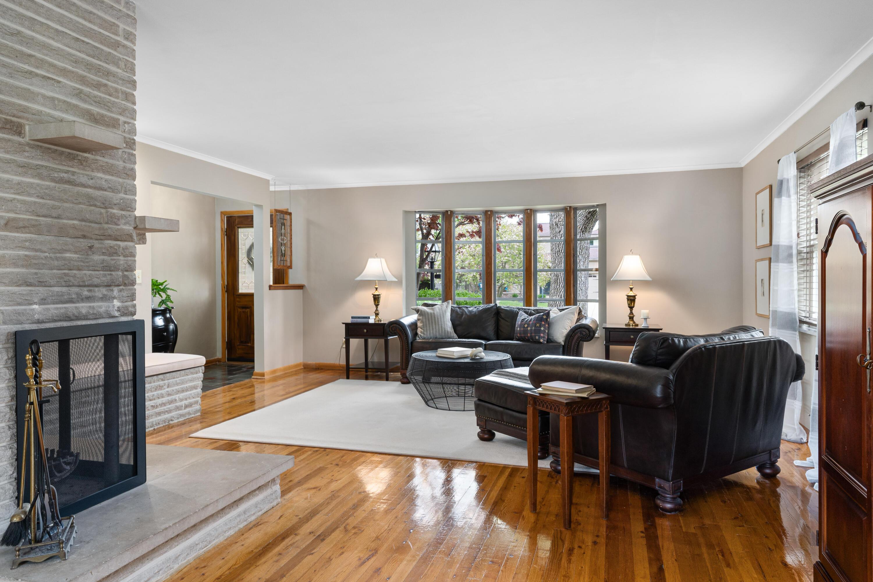 Living room with a stone fireplace, leather seating, hardwood floors, and a large window.
