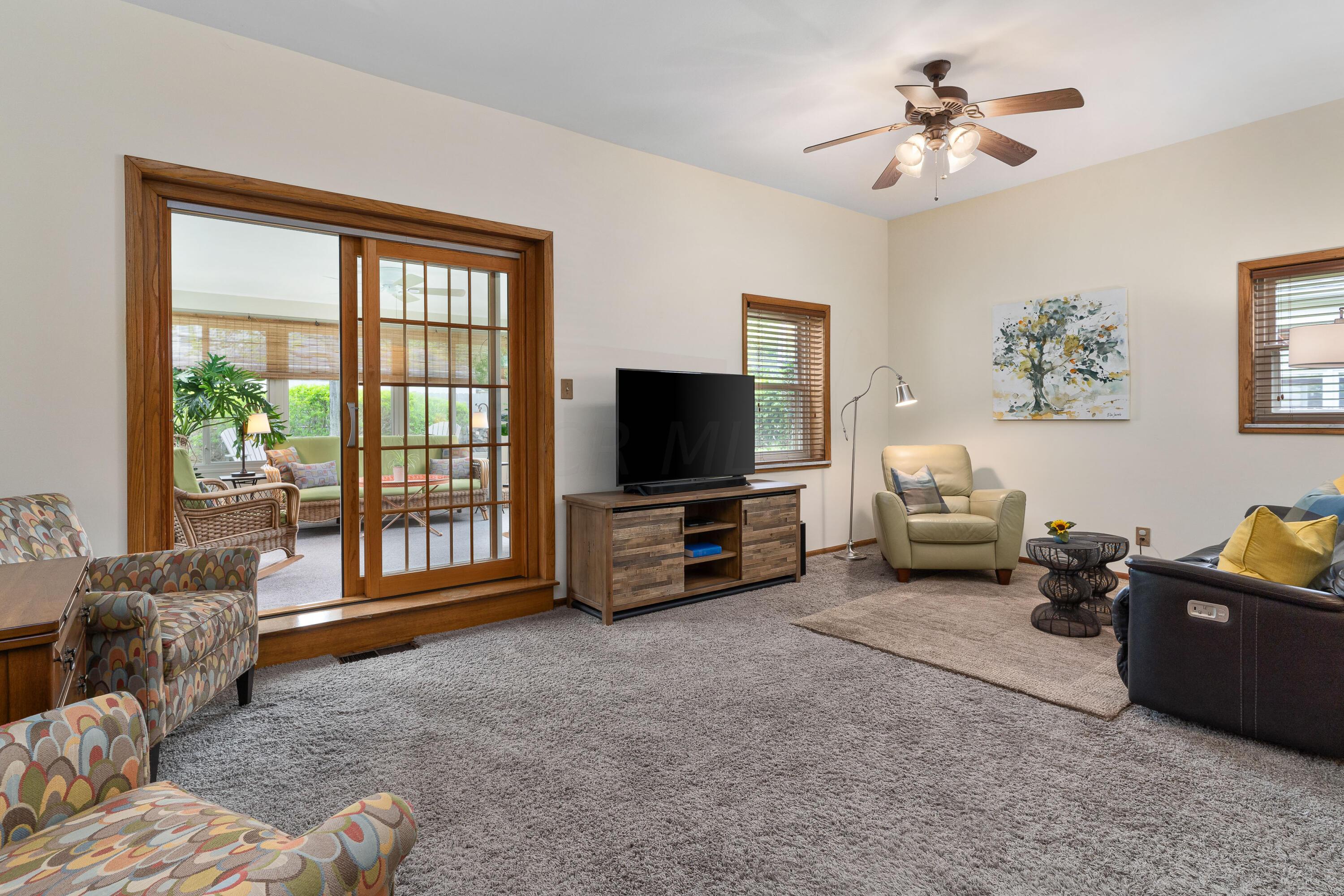 Living room with wood-framed sliding doors opening to a bright sunroom and a TV on a wooden console.