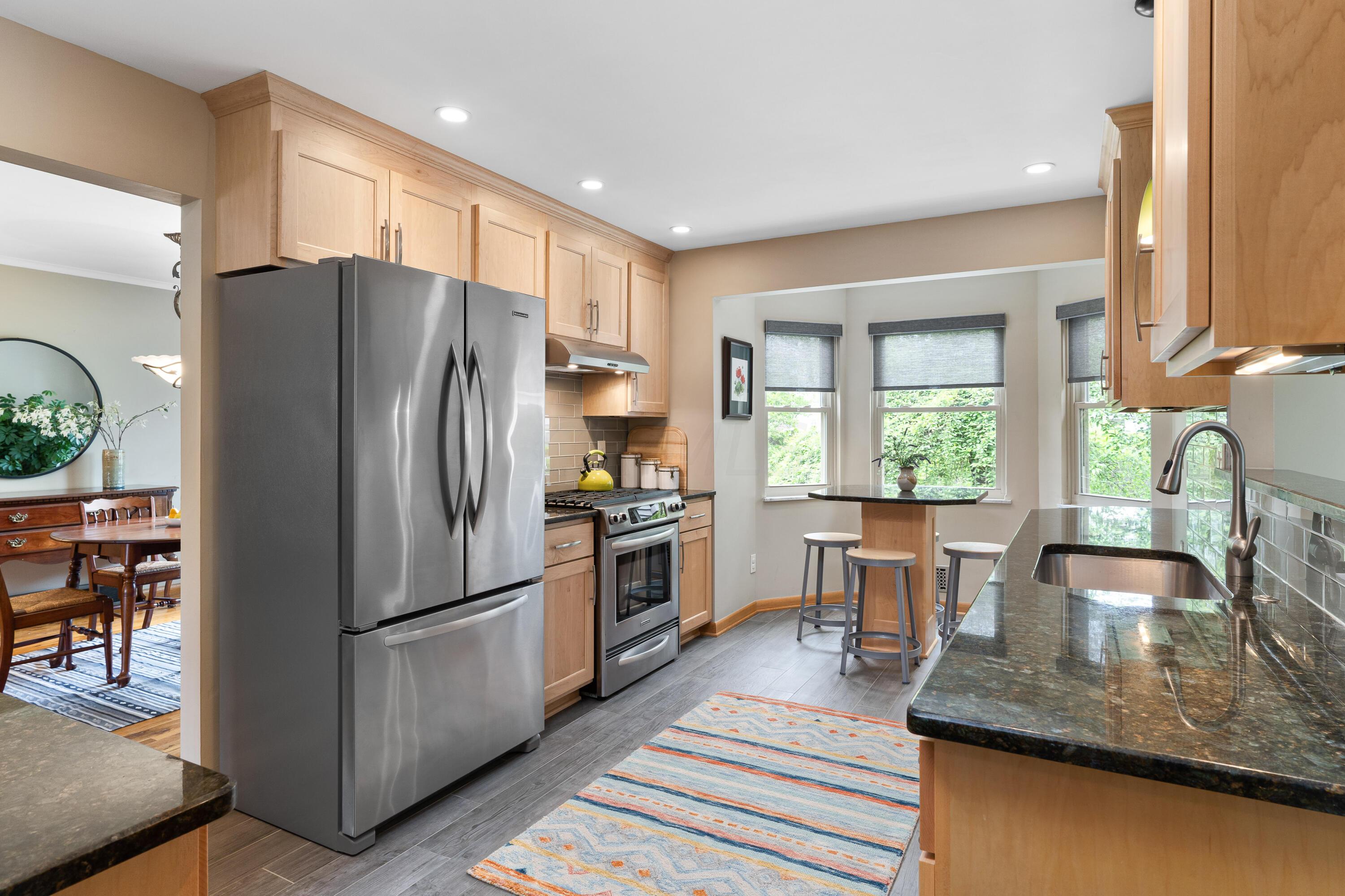 Kitchen with light wood cabinets, stainless appliances, granite island, and a window-side breakfast nook.