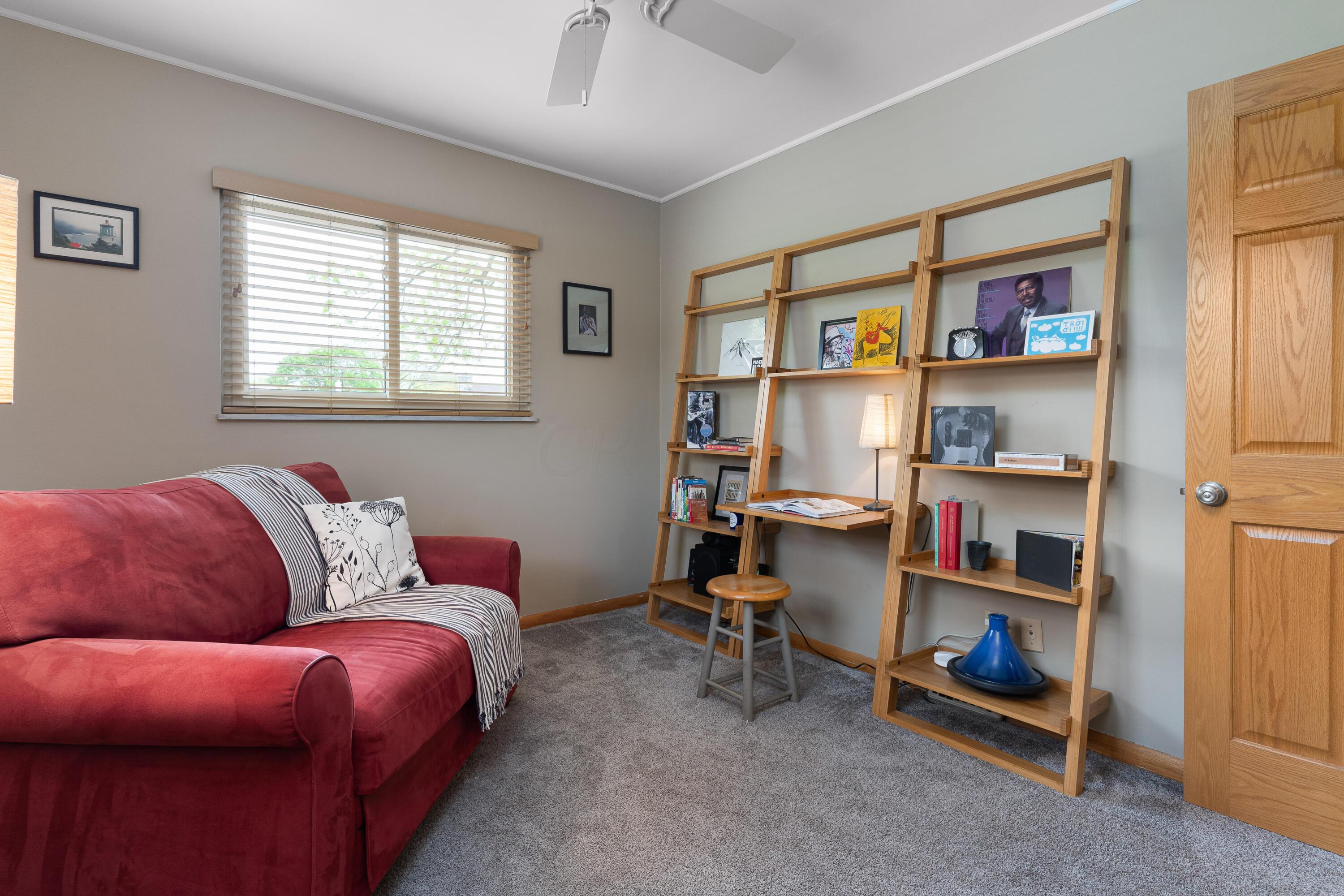 Furnished living room with a red sofa, gray carpet, and wooden shelving with a small desk.