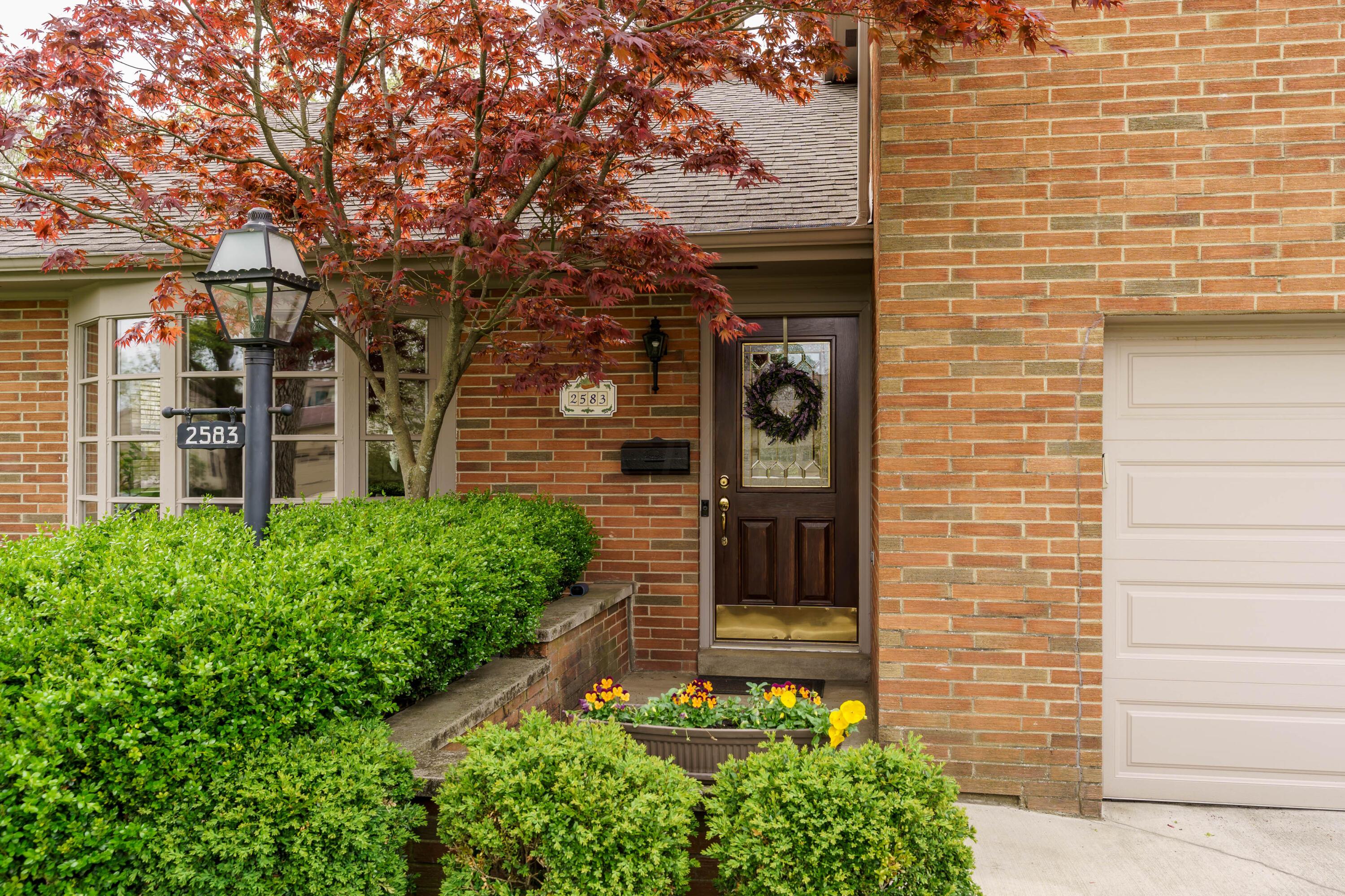 Brick home entrance with a dark wood door, autumn foliage, and landscaped shrubs.
