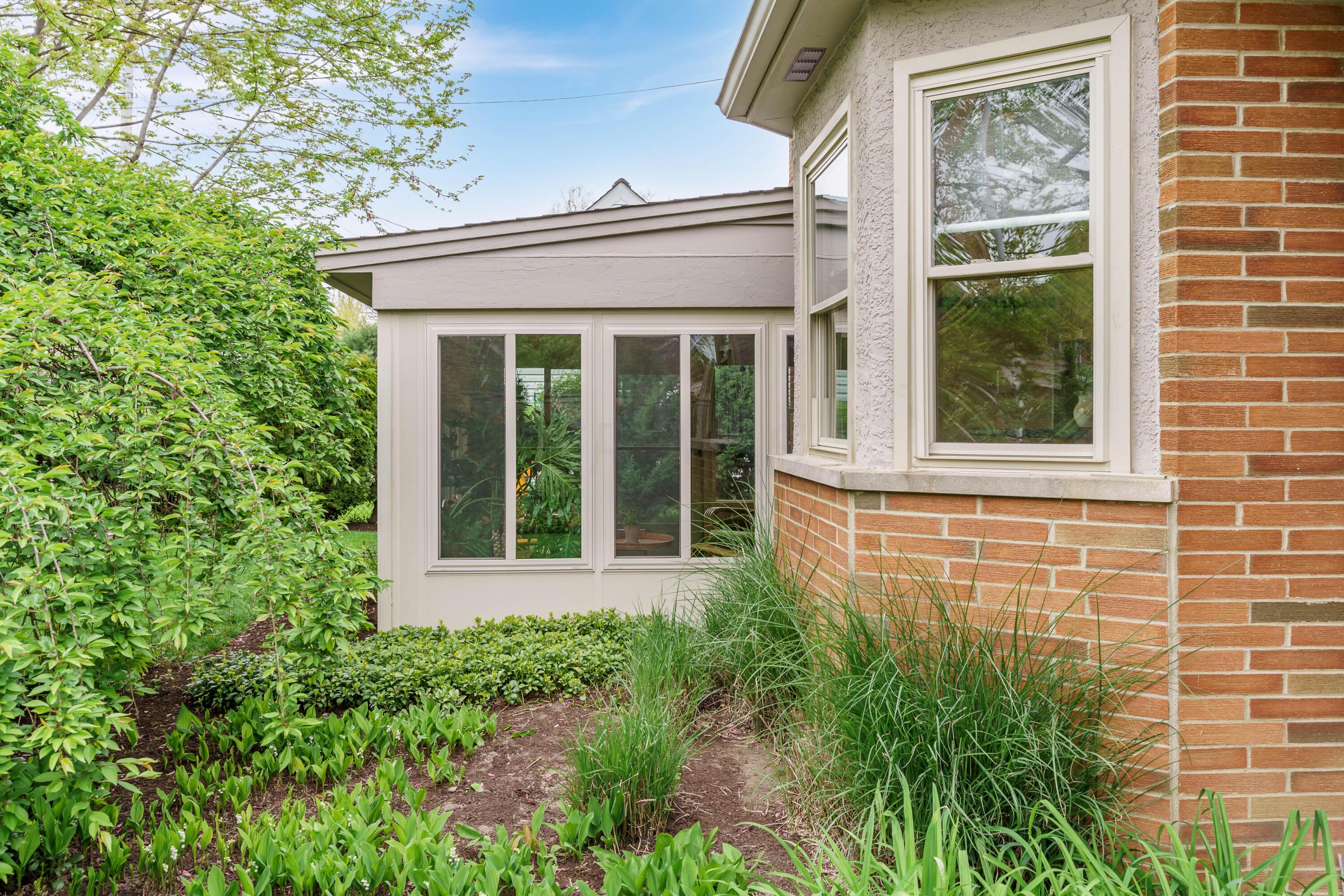 Home’s brick and stucco exterior with a bay window, sunroom, and lush garden.