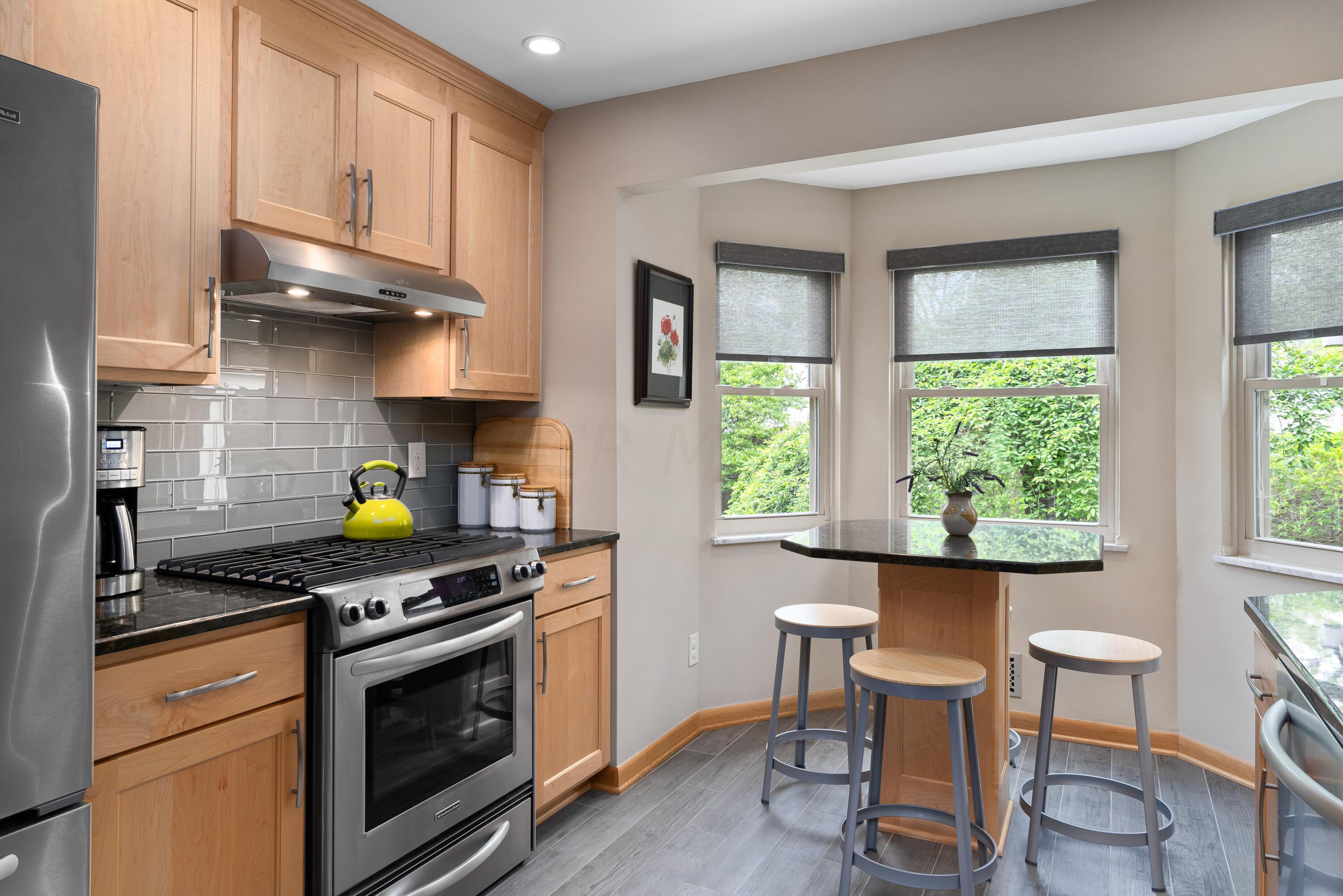 Kitchen with light wood cabinetry, stainless appliances, and a breakfast bar beside bright windows.