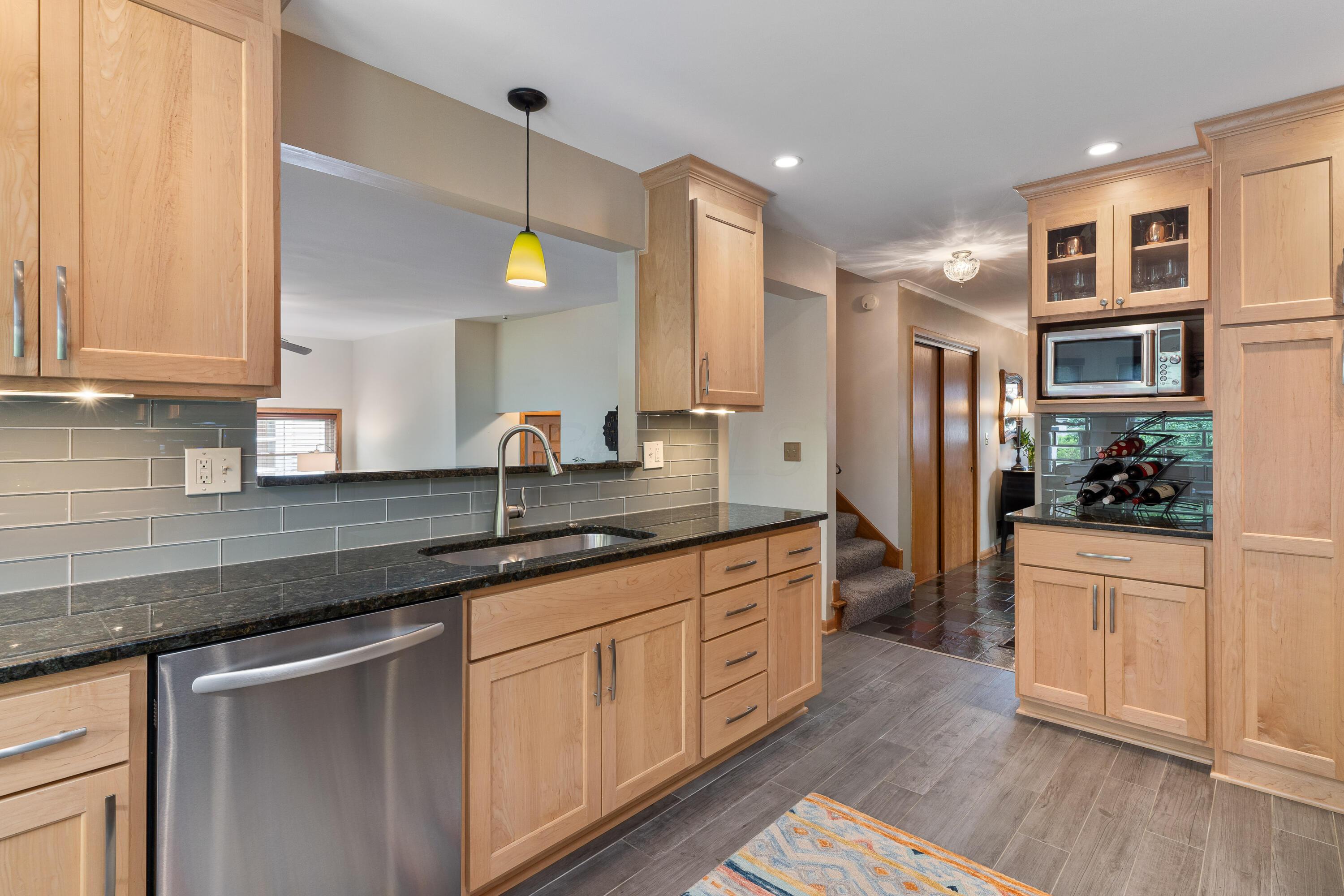 Kitchen with light wood cabinets, dark countertops, gray tile backsplash, and a built-in wine rack.