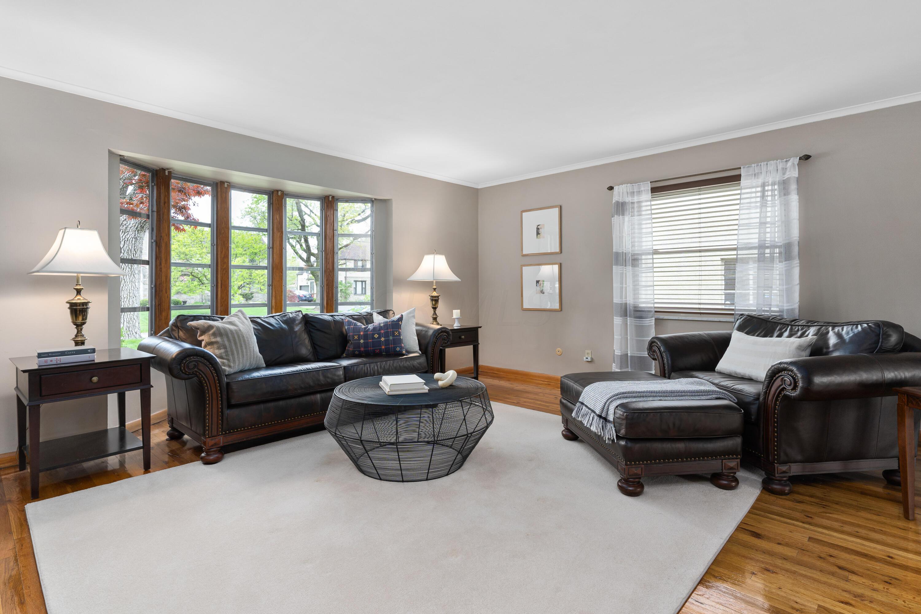 Living room with dark leather sofas, round wire coffee table, and a large bay window.