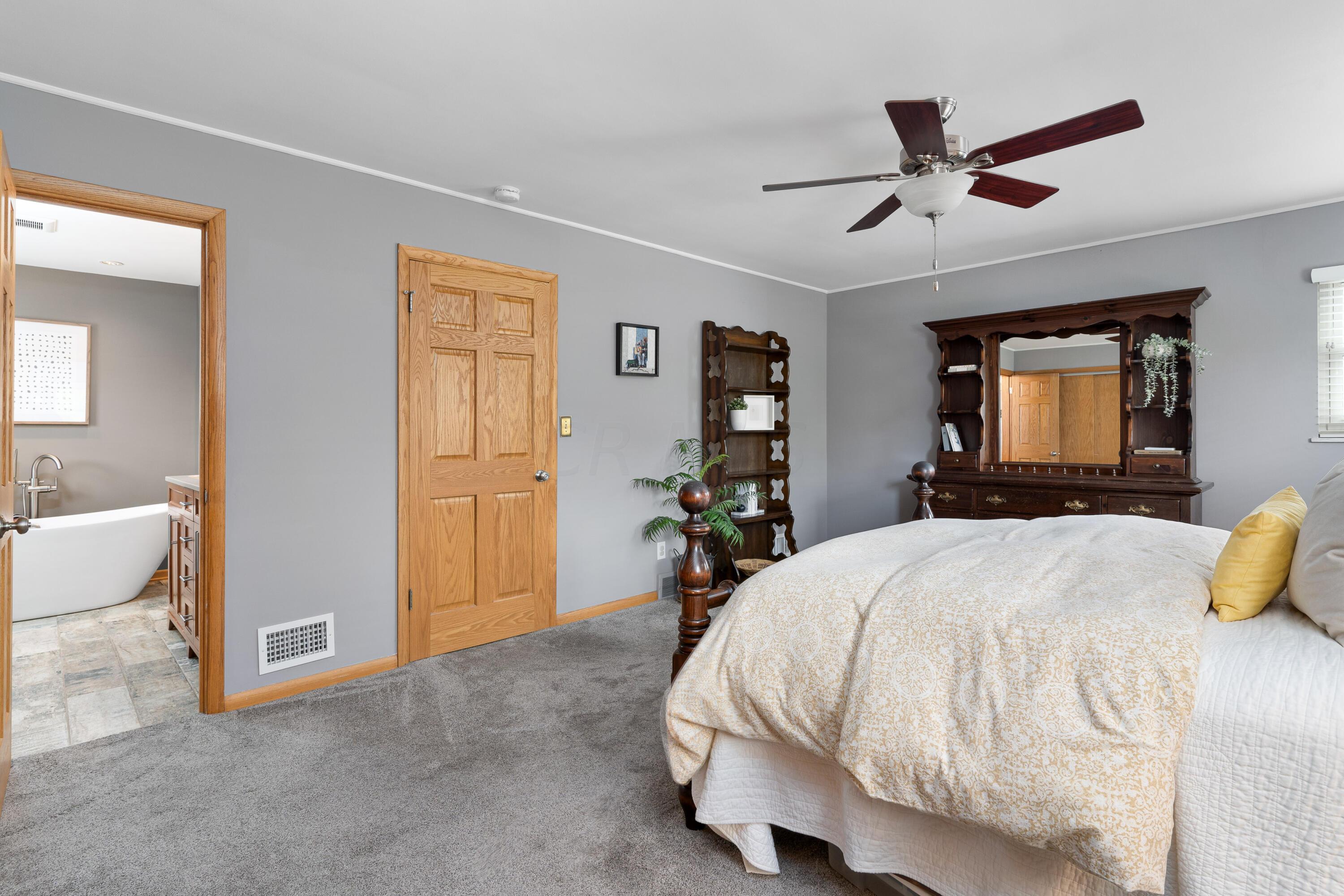 Bedroom with a large patterned bed, dark wood dresser and mirror, and adjoining bathroom.