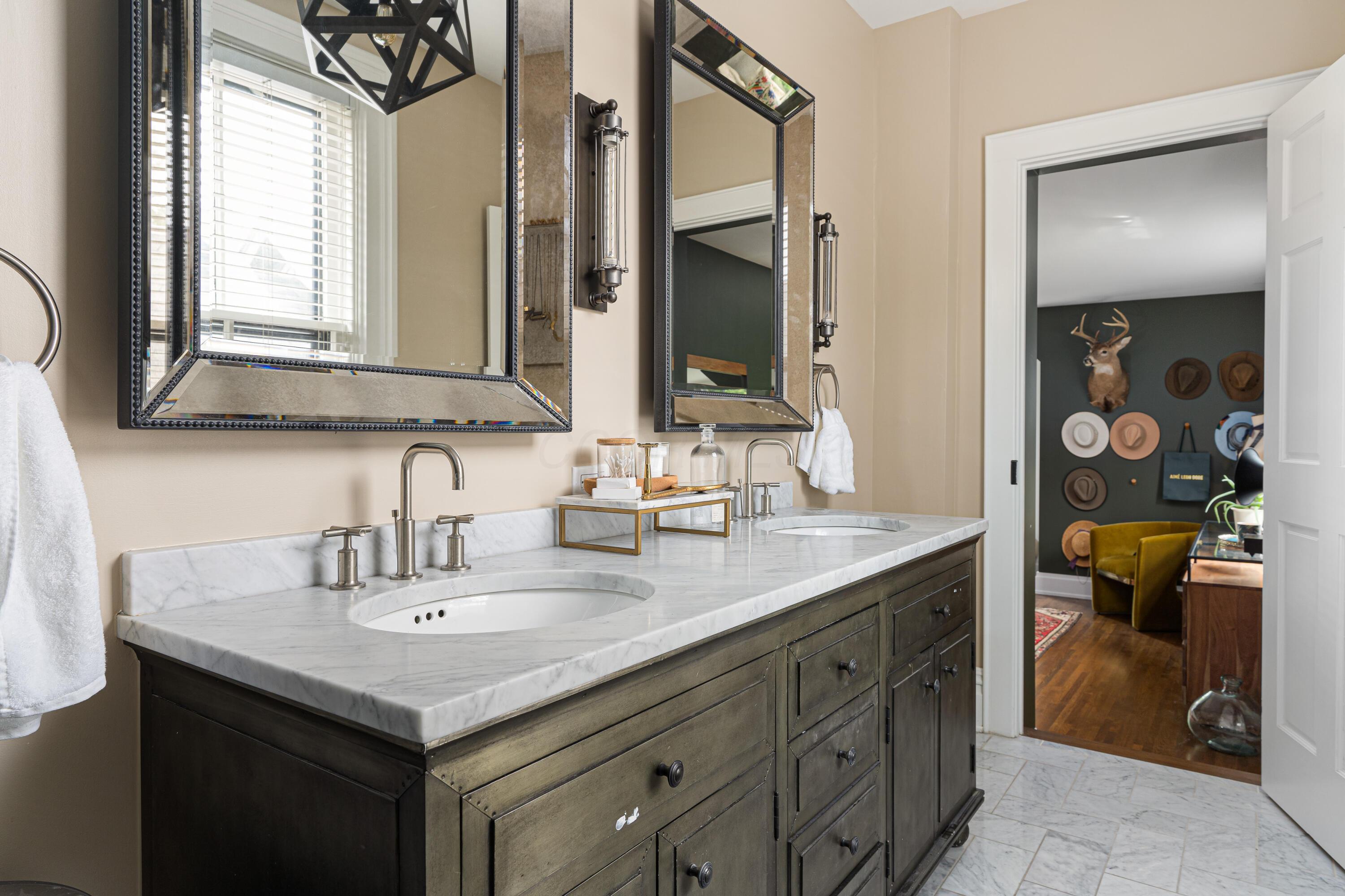 Bathroom with a marble double vanity, dark wood cabinetry, and large mirrors opening onto a sitting room.