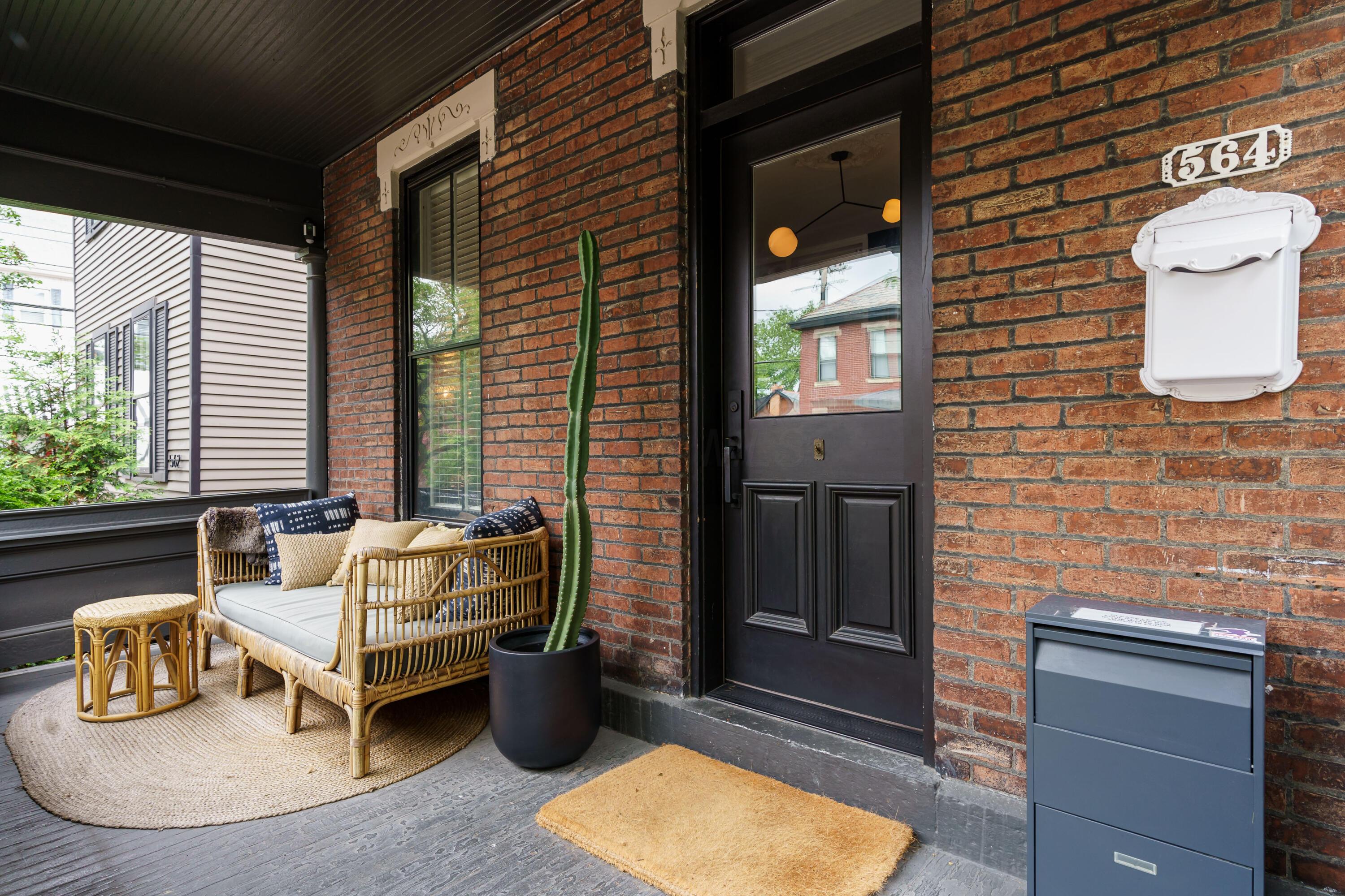 Covered brick front porch with wicker seating, a potted cactus, and black entry door marked 564.