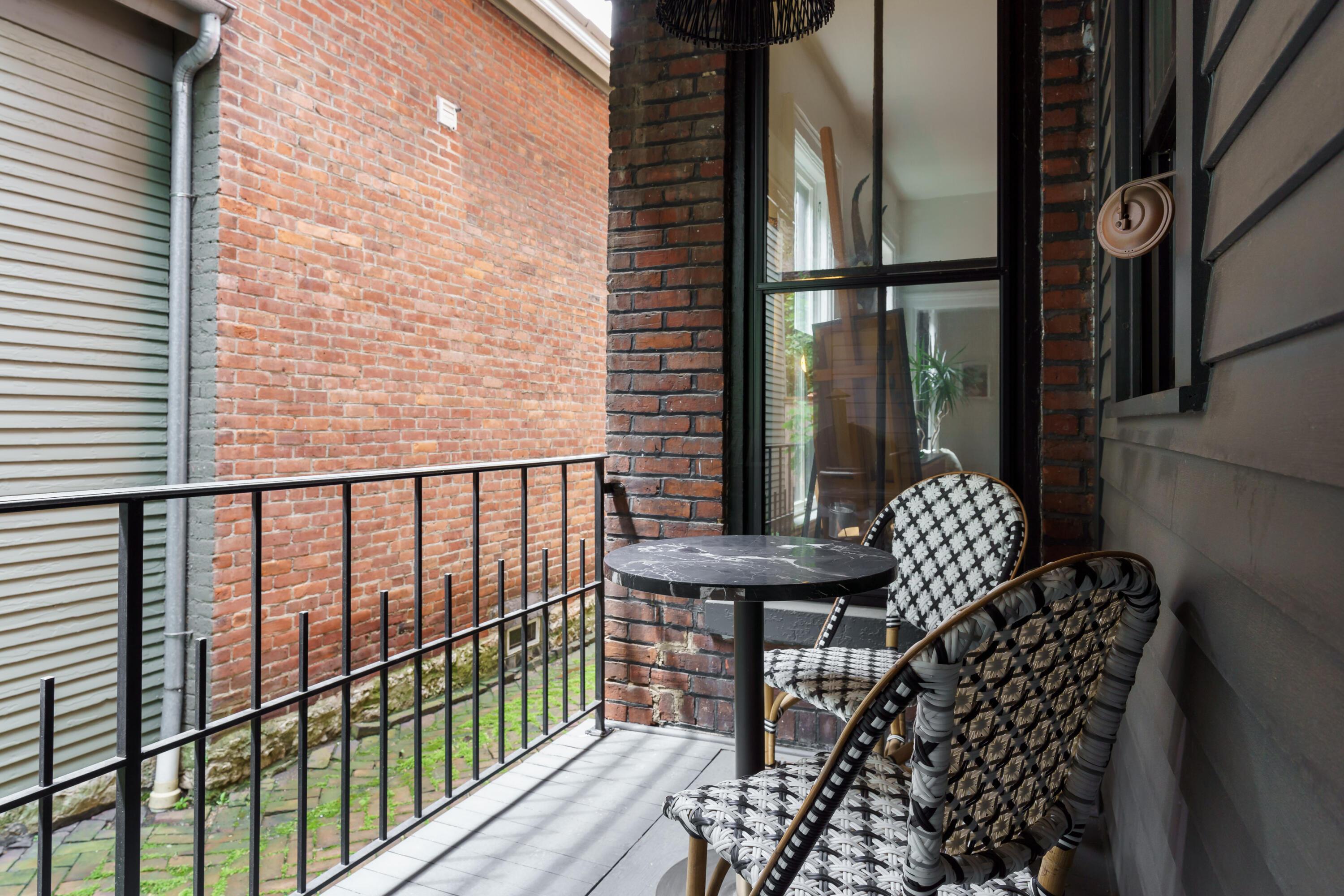 Balcony with woven chairs and a round table beside a brick wall.
