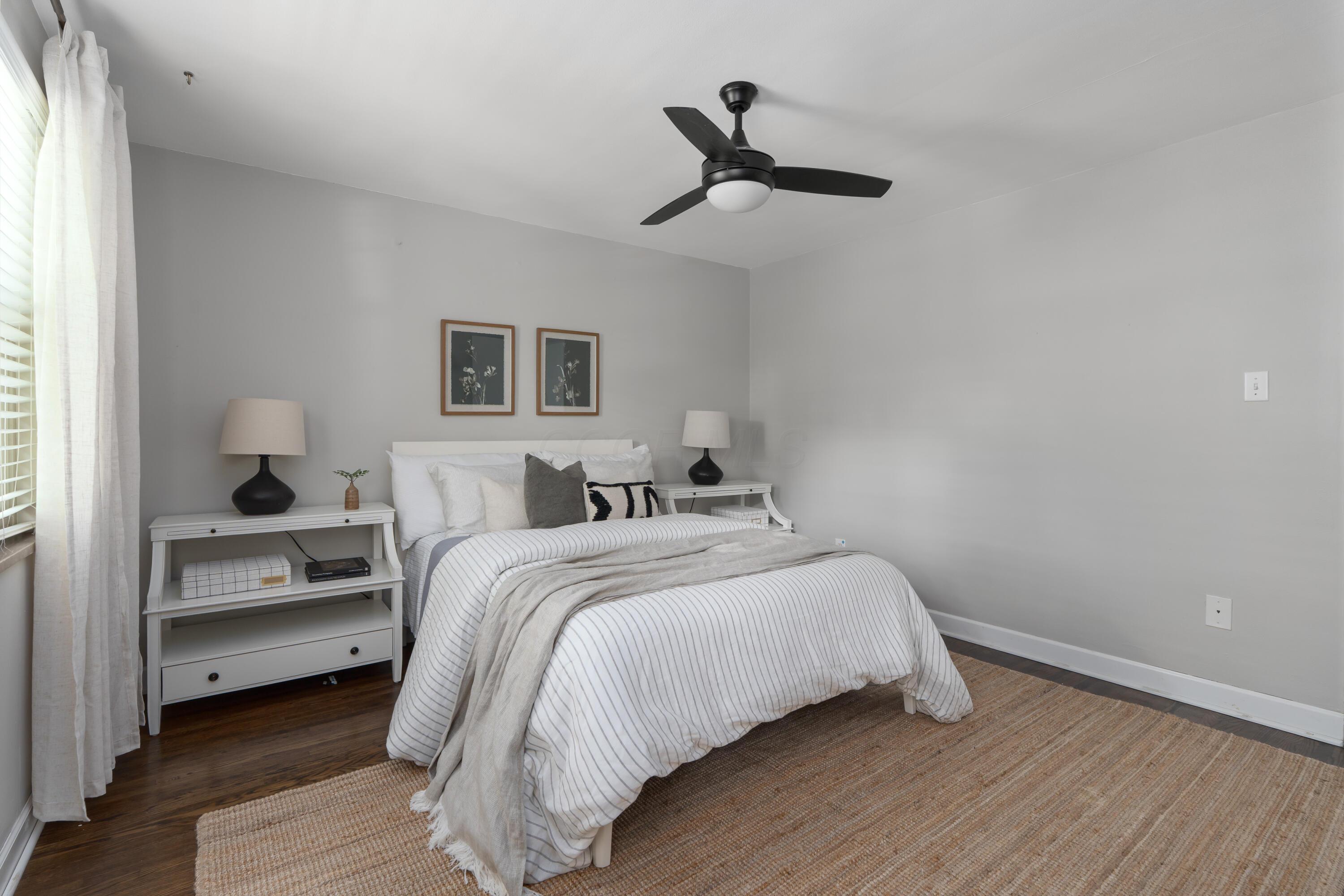 Staged bedroom with striped white bedding, gray walls, and a black ceiling fan.