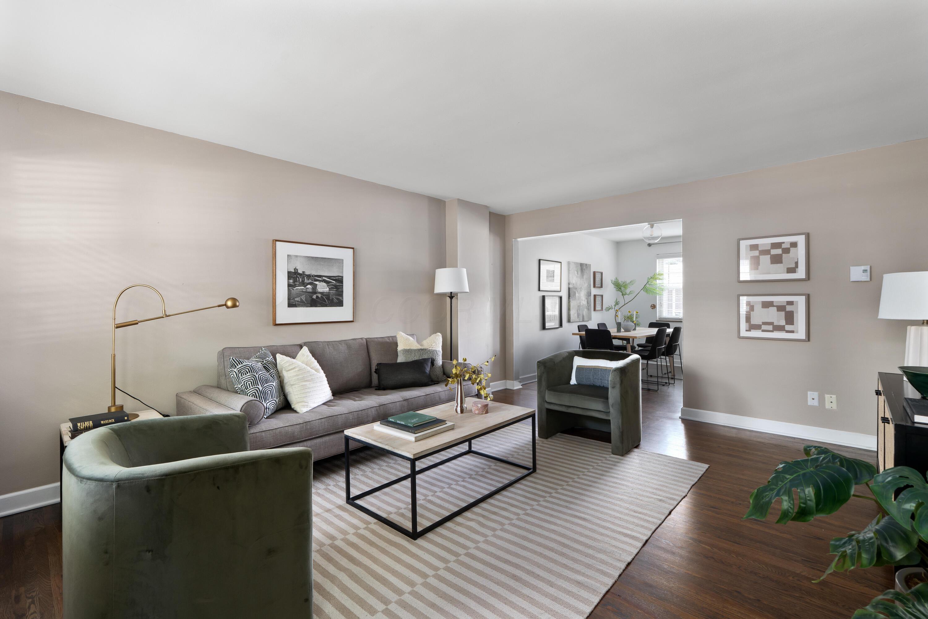 Staged living room with gray sofa, green armchairs, and an open view into the dining area.