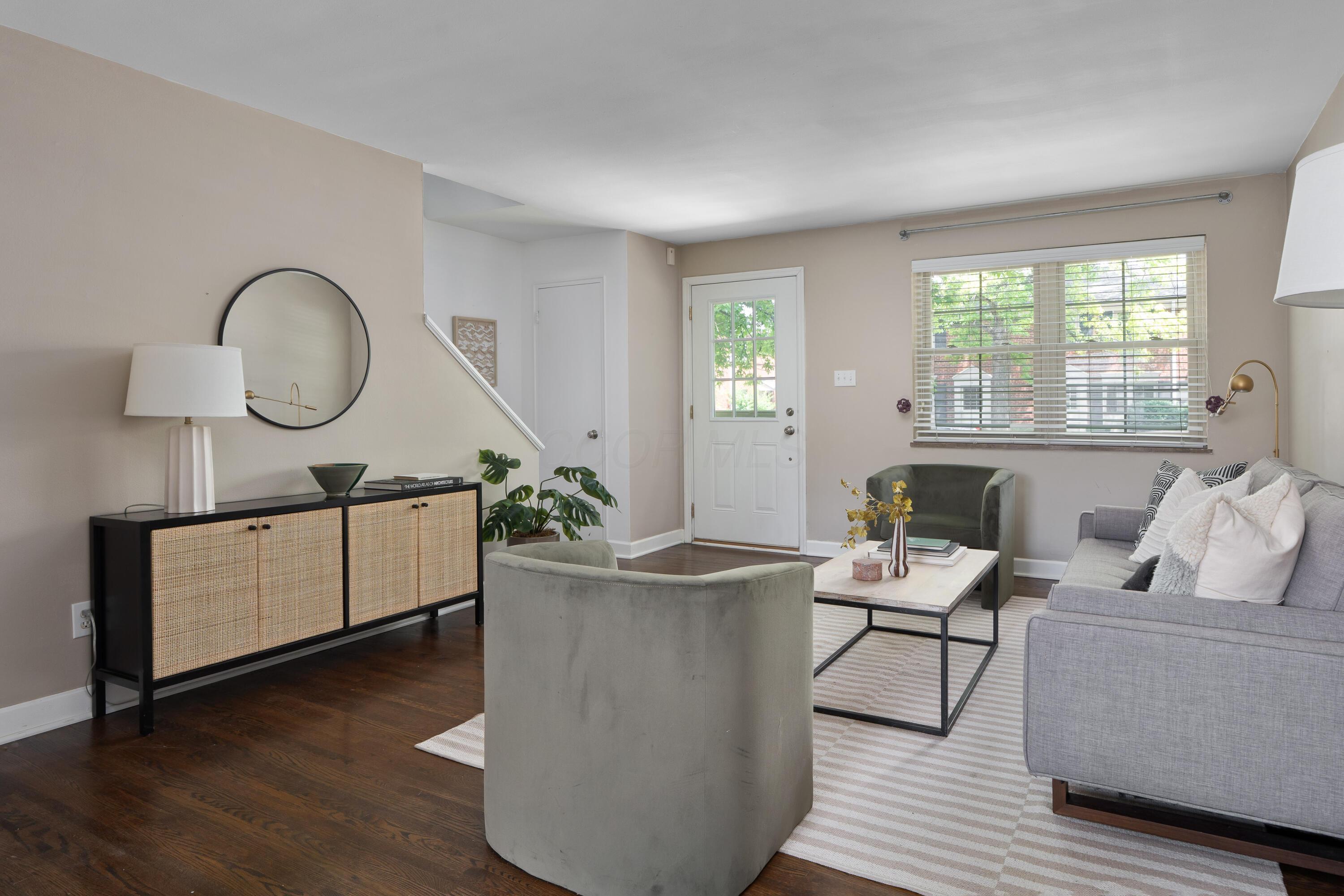 Furnished living room with a gray sofa, green armchairs, and a large window beside the entry door.