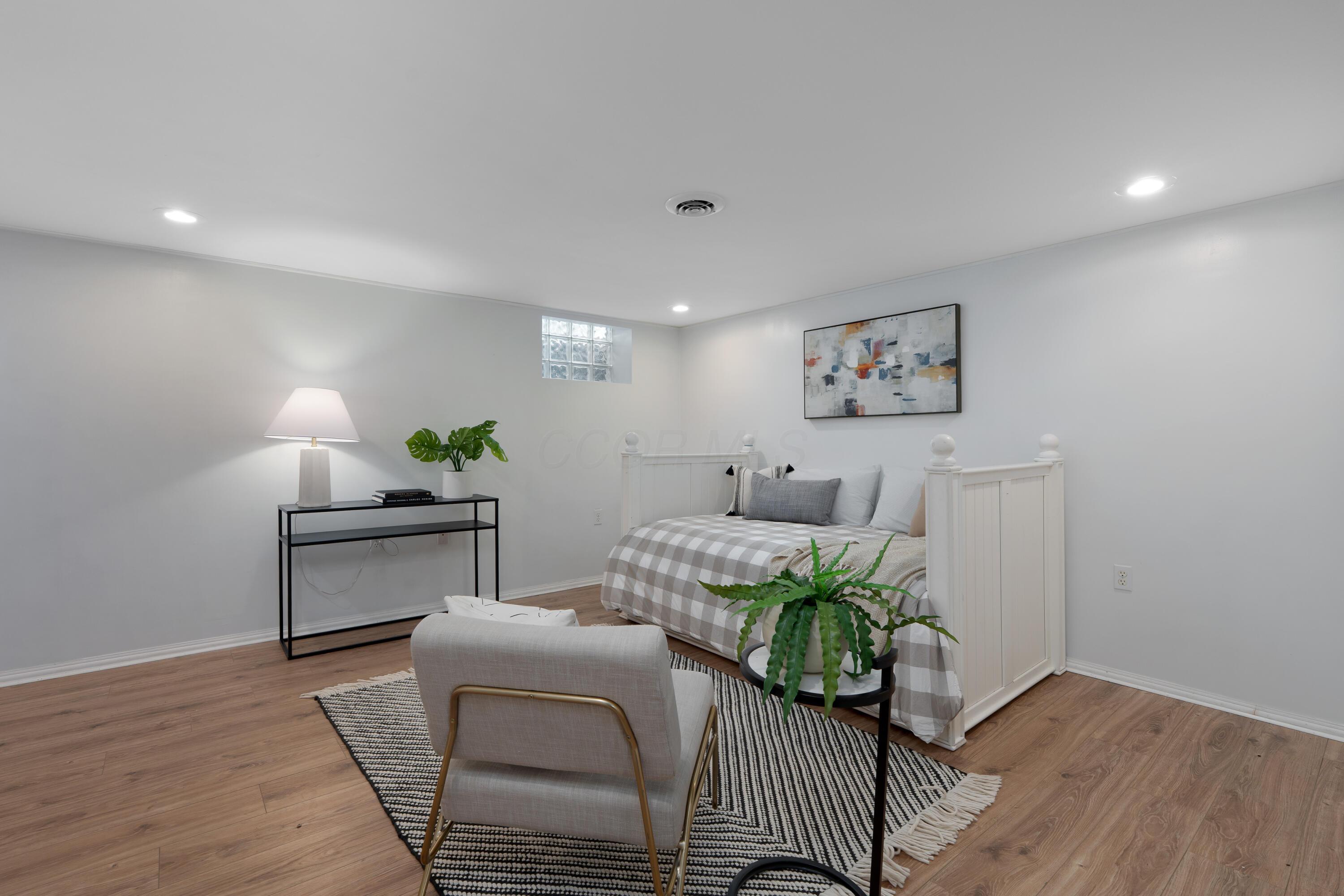 Staged bedroom with a white spindle bed, checked bedding, wood-look floors, and a striped rug.