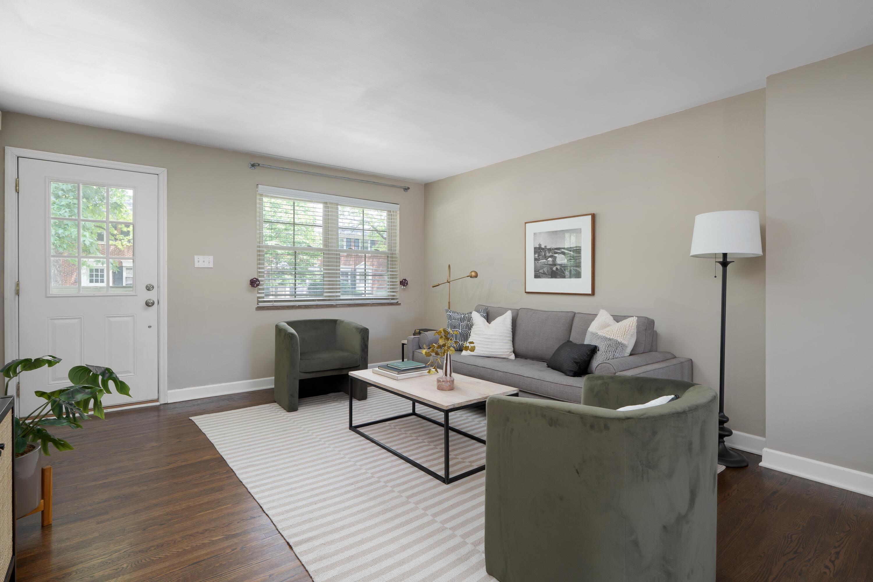 Staged living room with a gray sofa, olive-green armchairs, striped rug, and daylight through the window.