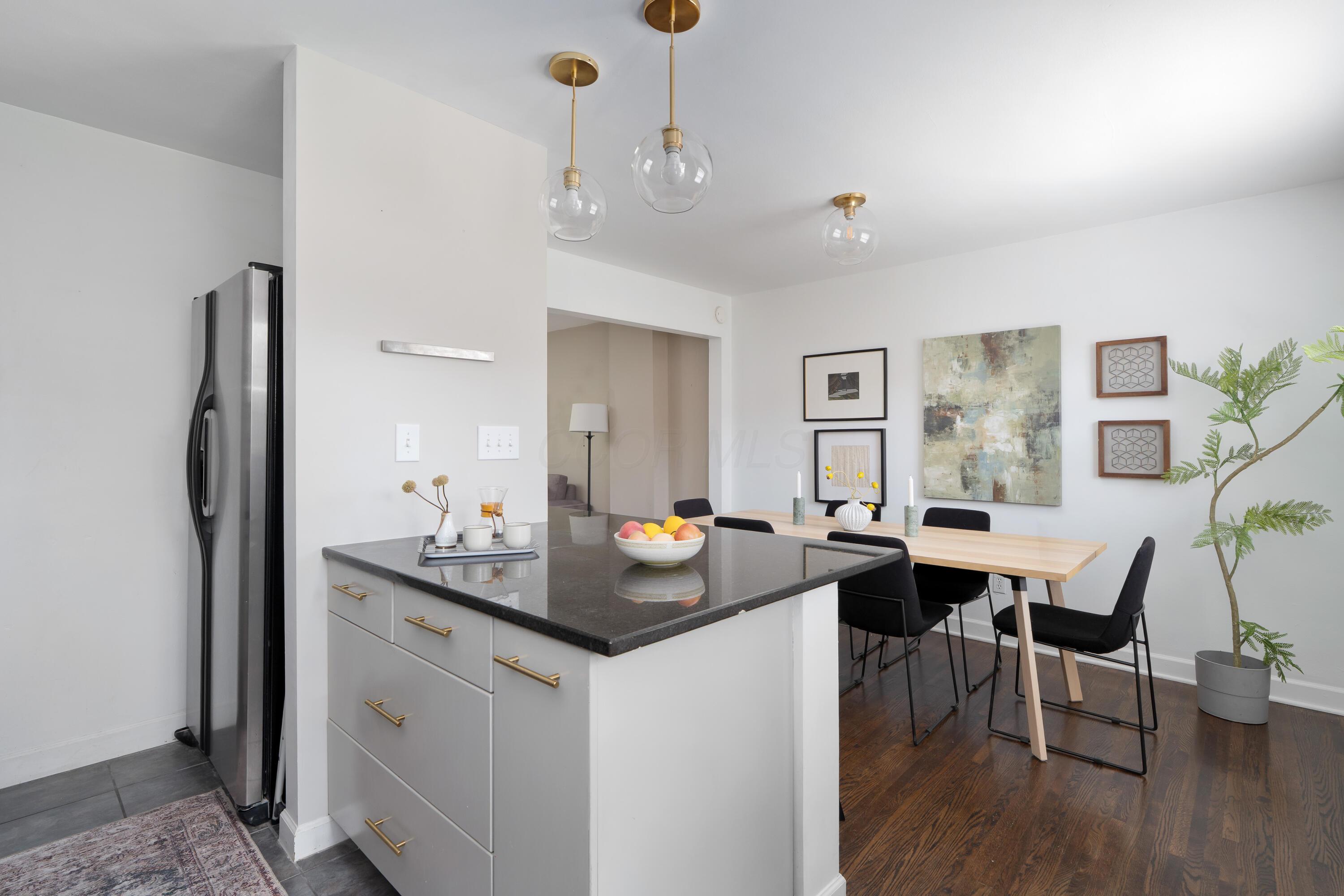 Open-plan kitchen with a dark stone island beside a light wood dining table and black chairs.
