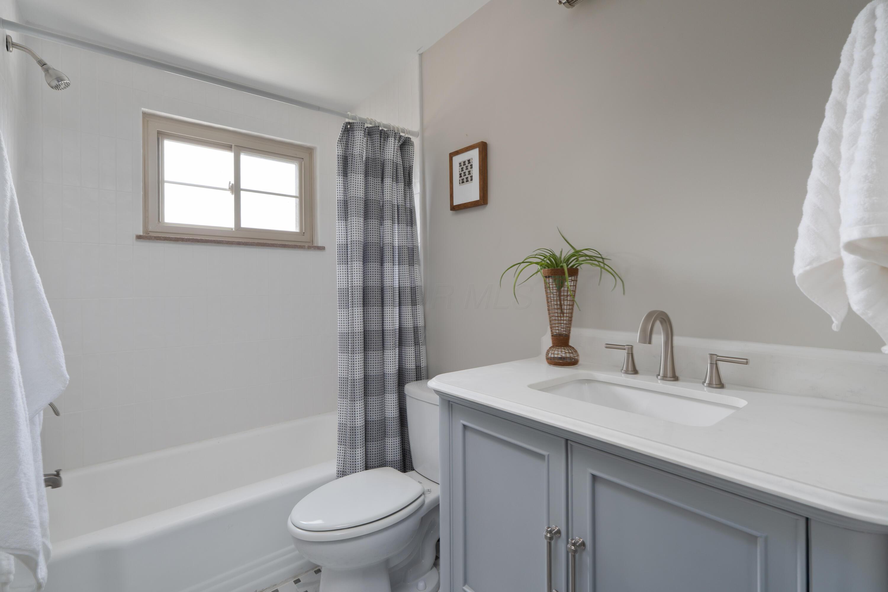 Bathroom with a white tub, window, patterned shower curtain, and gray vanity.