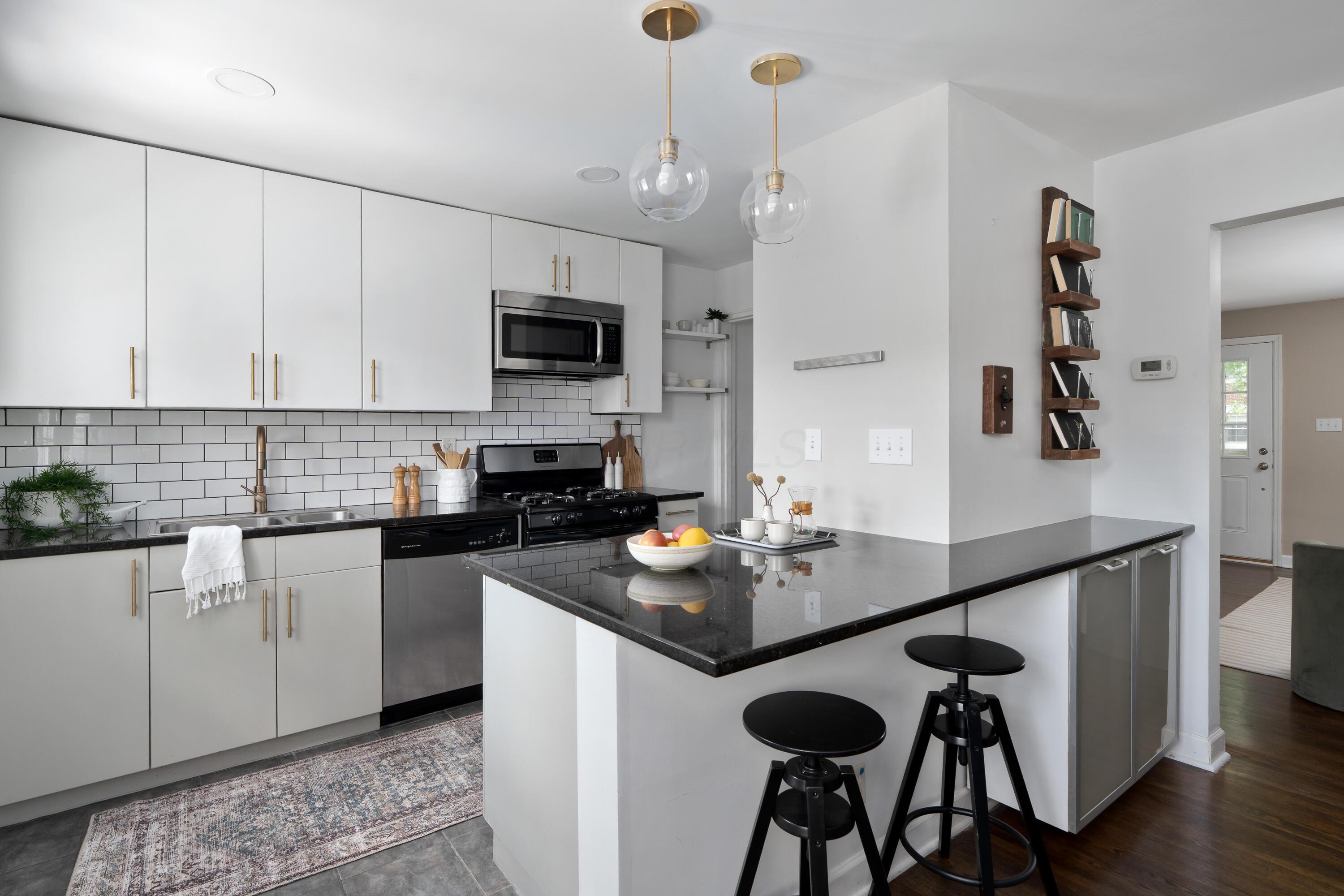 Modern white kitchen with a black stone island, two stools, and brass-accented pendant lights.