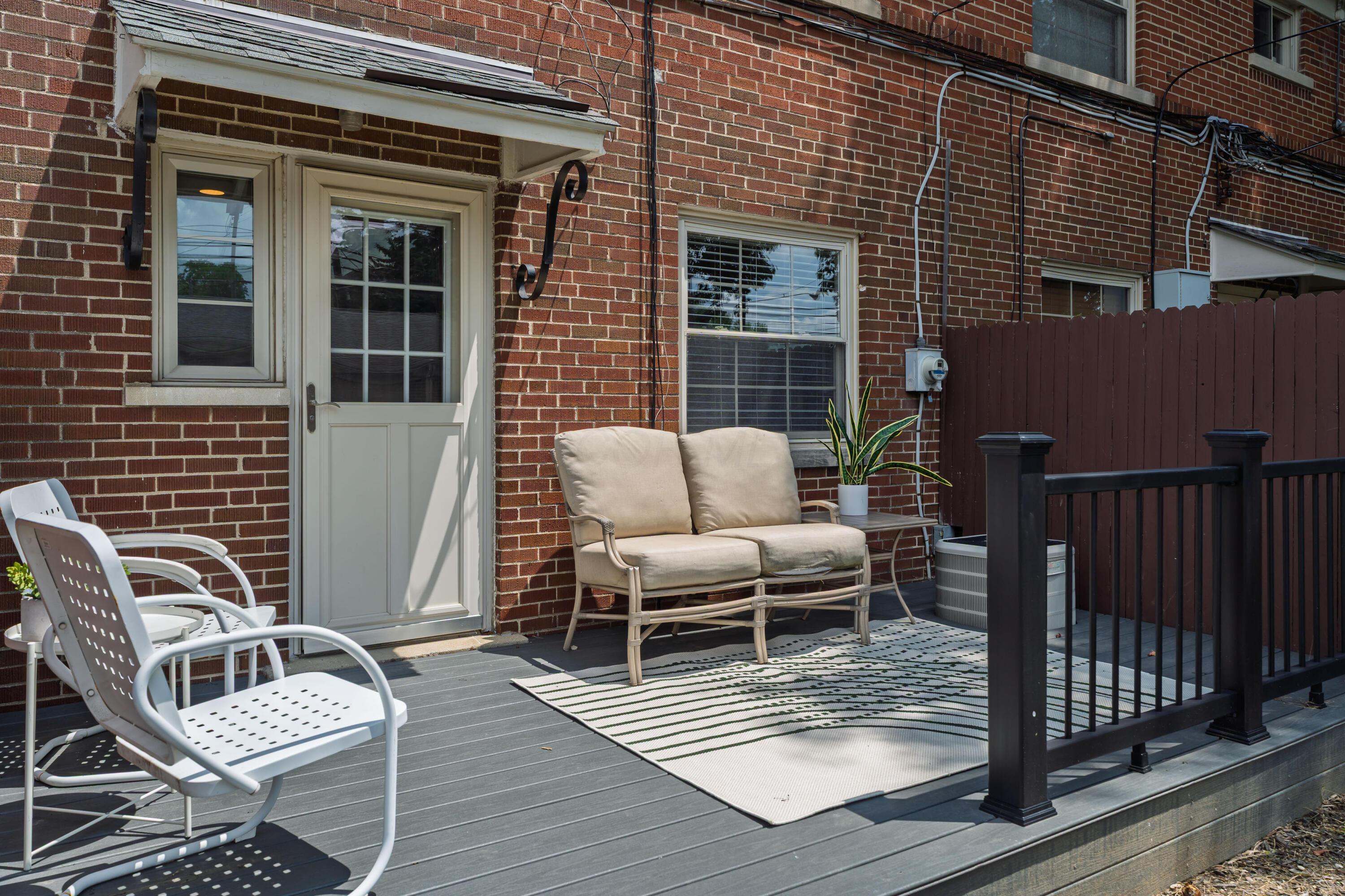 Raised deck with outdoor seating, a patterned rug, and a red brick wall.