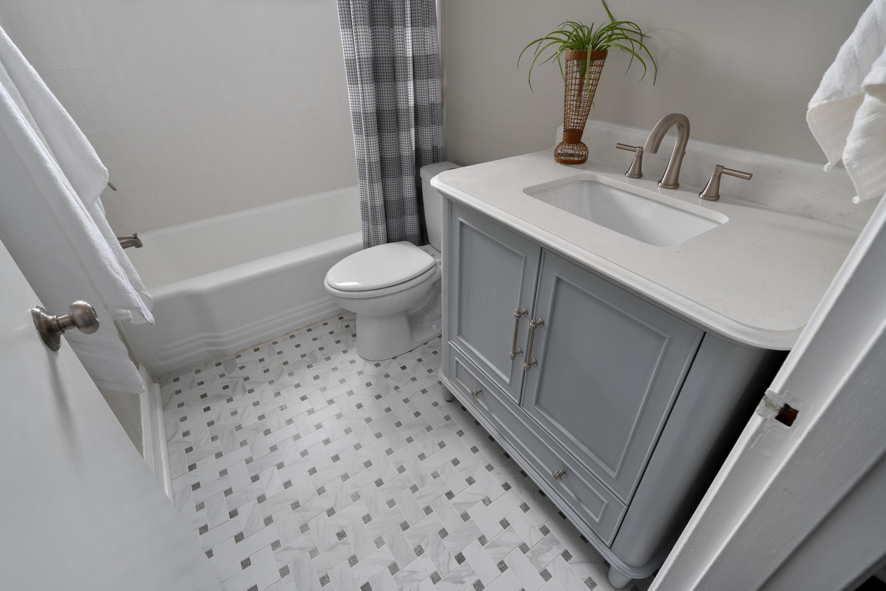 Bathroom with gray vanity, white sink, bathtub, and marble-look mosaic floor.