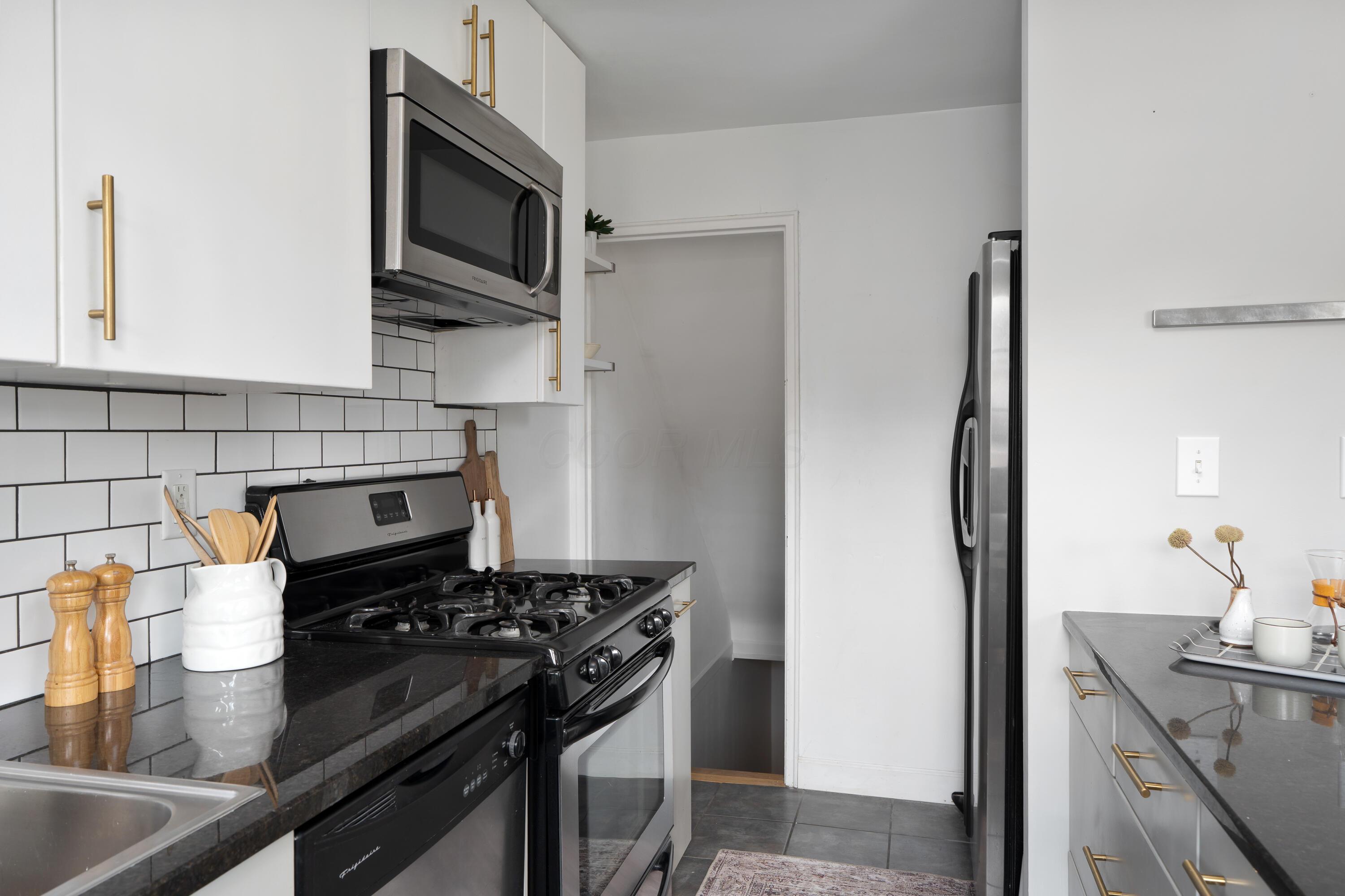 Renovated kitchen with white cabinets, black granite counters, subway tile backsplash, and stainless-steel appliances.