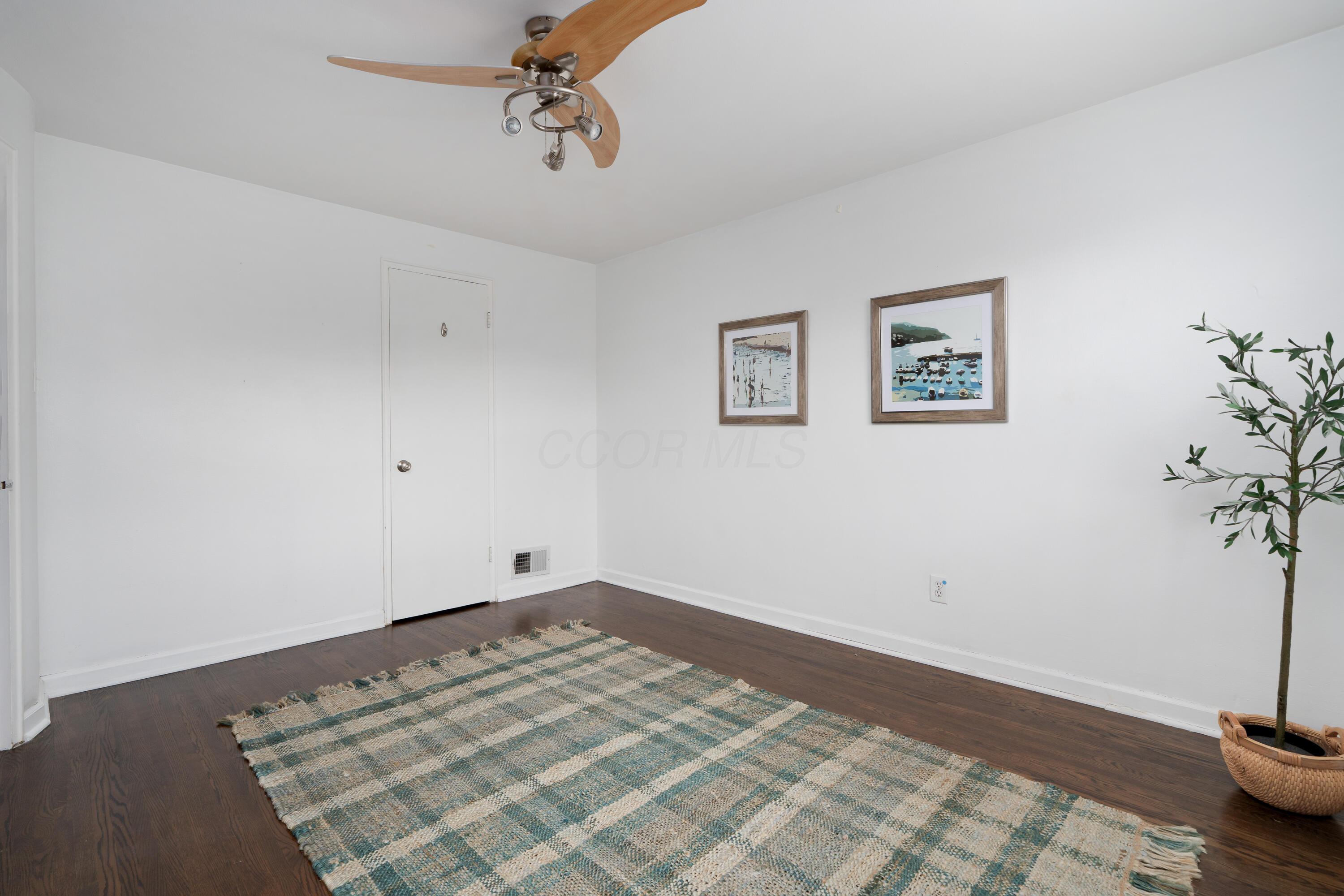 Room with dark hardwood floors, a patterned rug, ceiling fan, framed art, and potted tree.