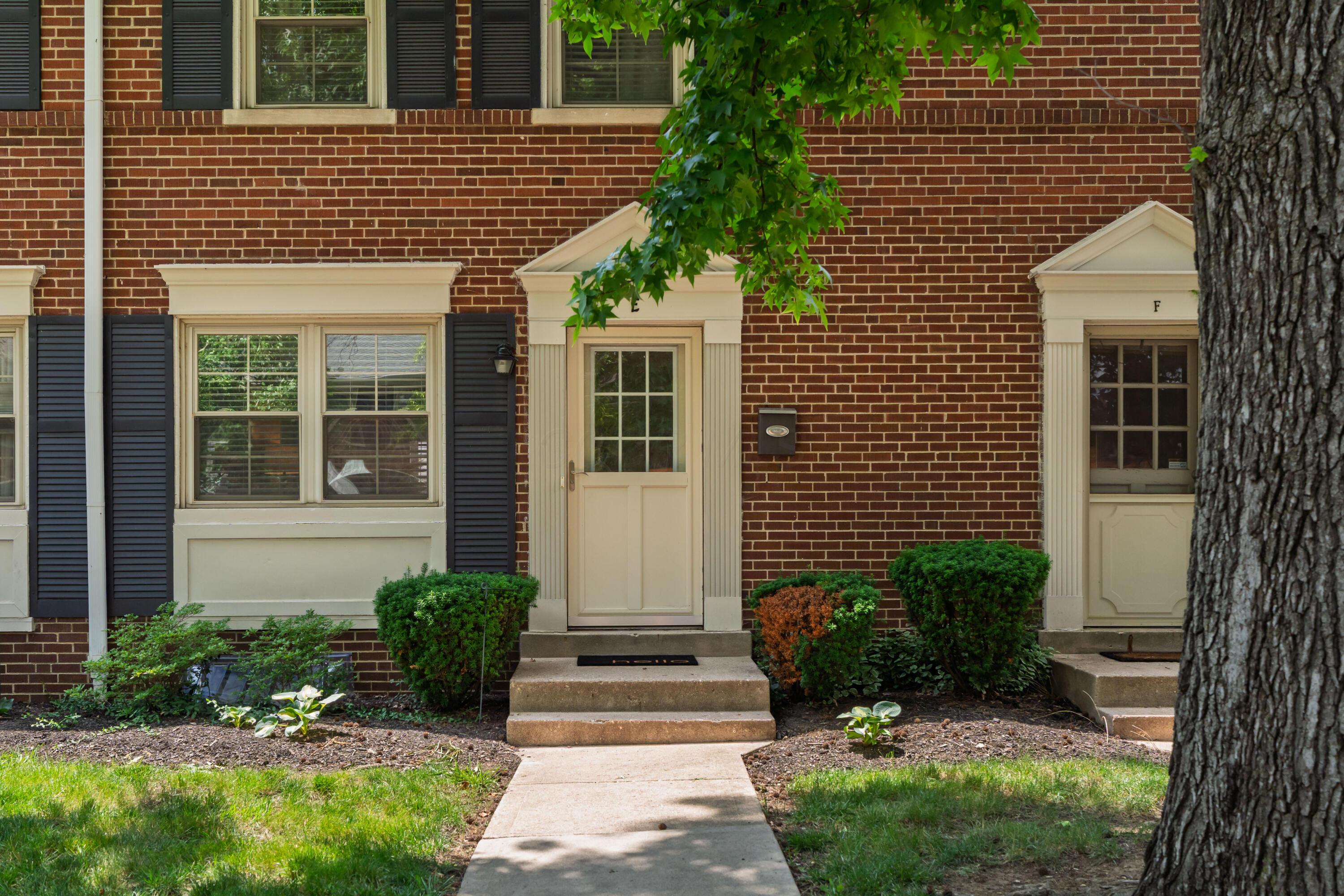 Red-brick townhouse entrance with cream door, concrete steps, and landscaped shrubs.