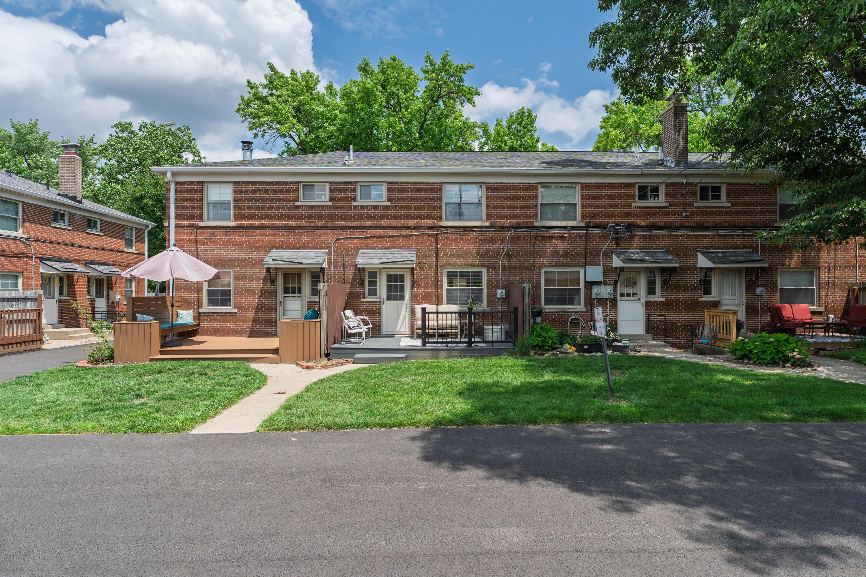 Rear of a brick residential building with several patios, outdoor seating, and a lawn.