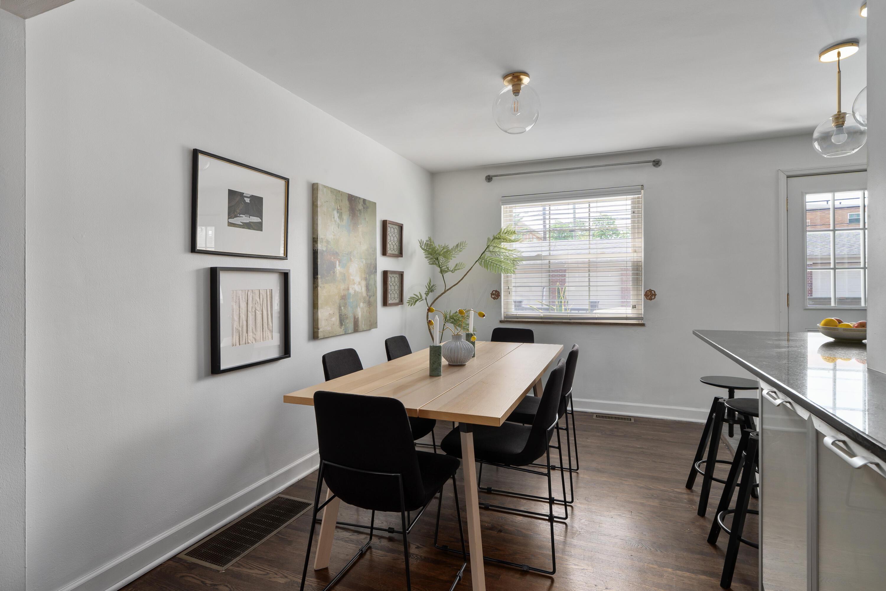 Dining area with a light-wood table, black chairs, framed art, and a kitchen island.