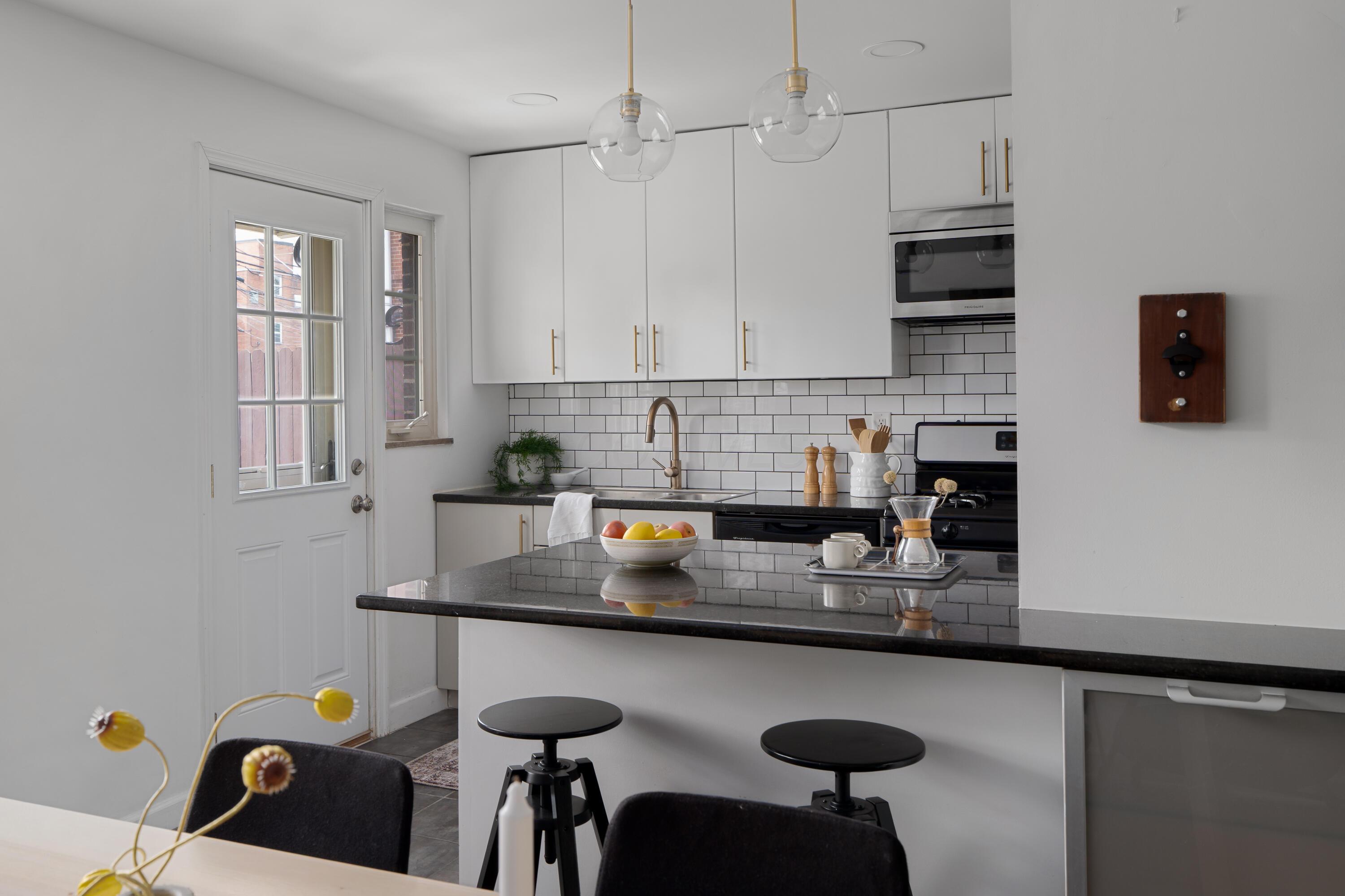Modern white kitchen with subway tile backsplash, black counters, and a peninsula with two stools.