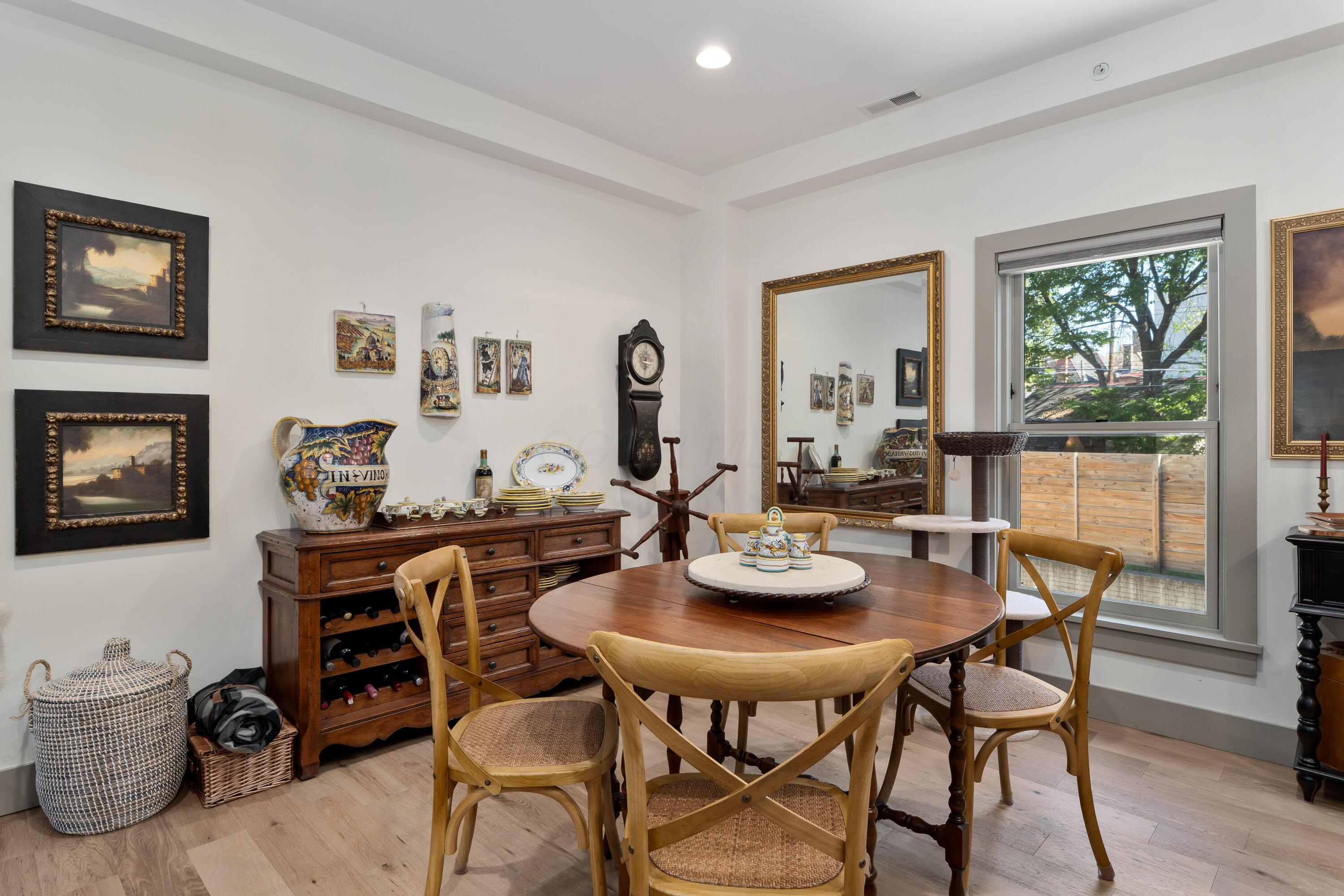 Dining room with a round wooden table, colorful ceramics, and a large window overlooking a tree.