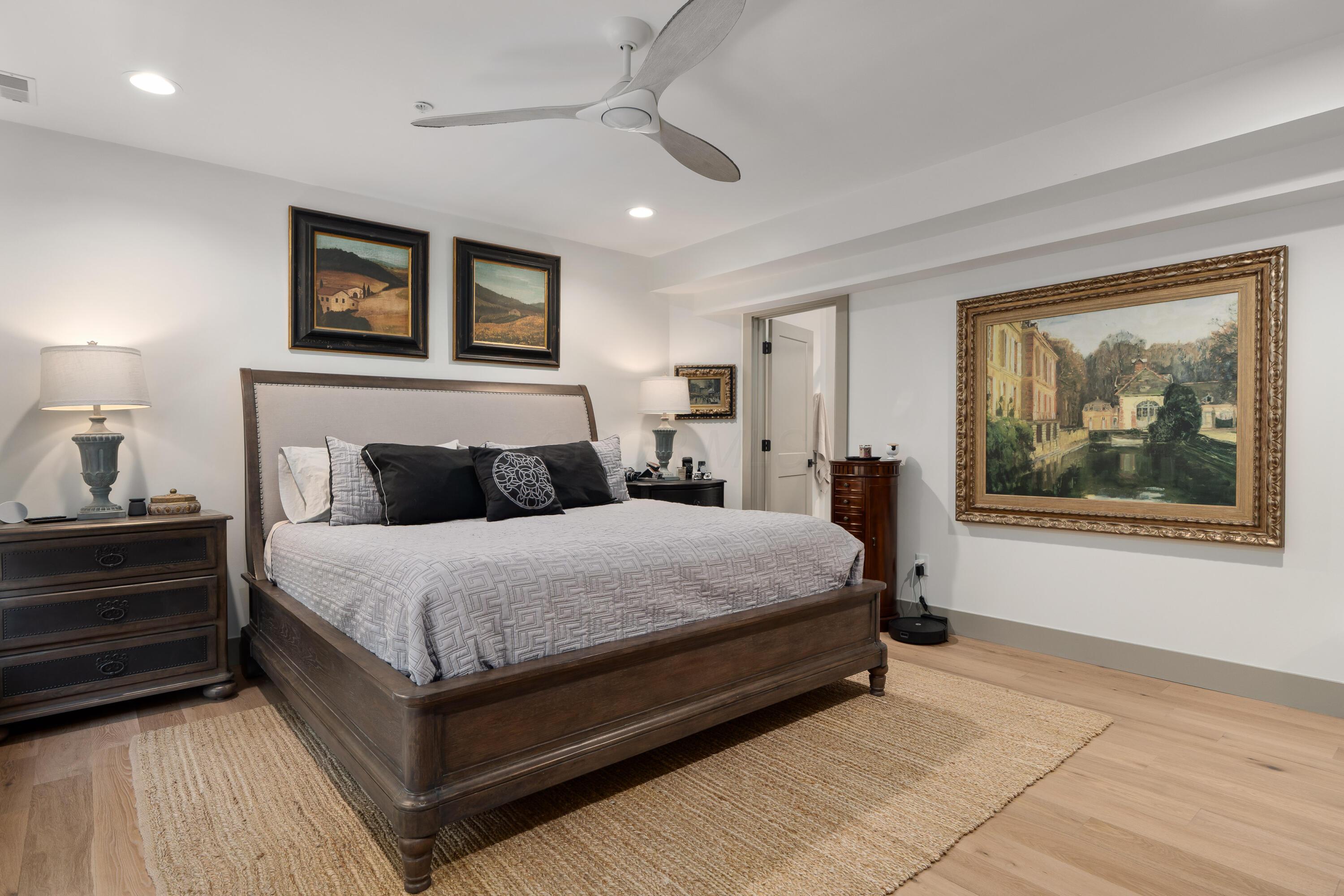 Furnished bedroom with a dark wood bed, patterned gray bedding, framed art, and a ceiling fan.