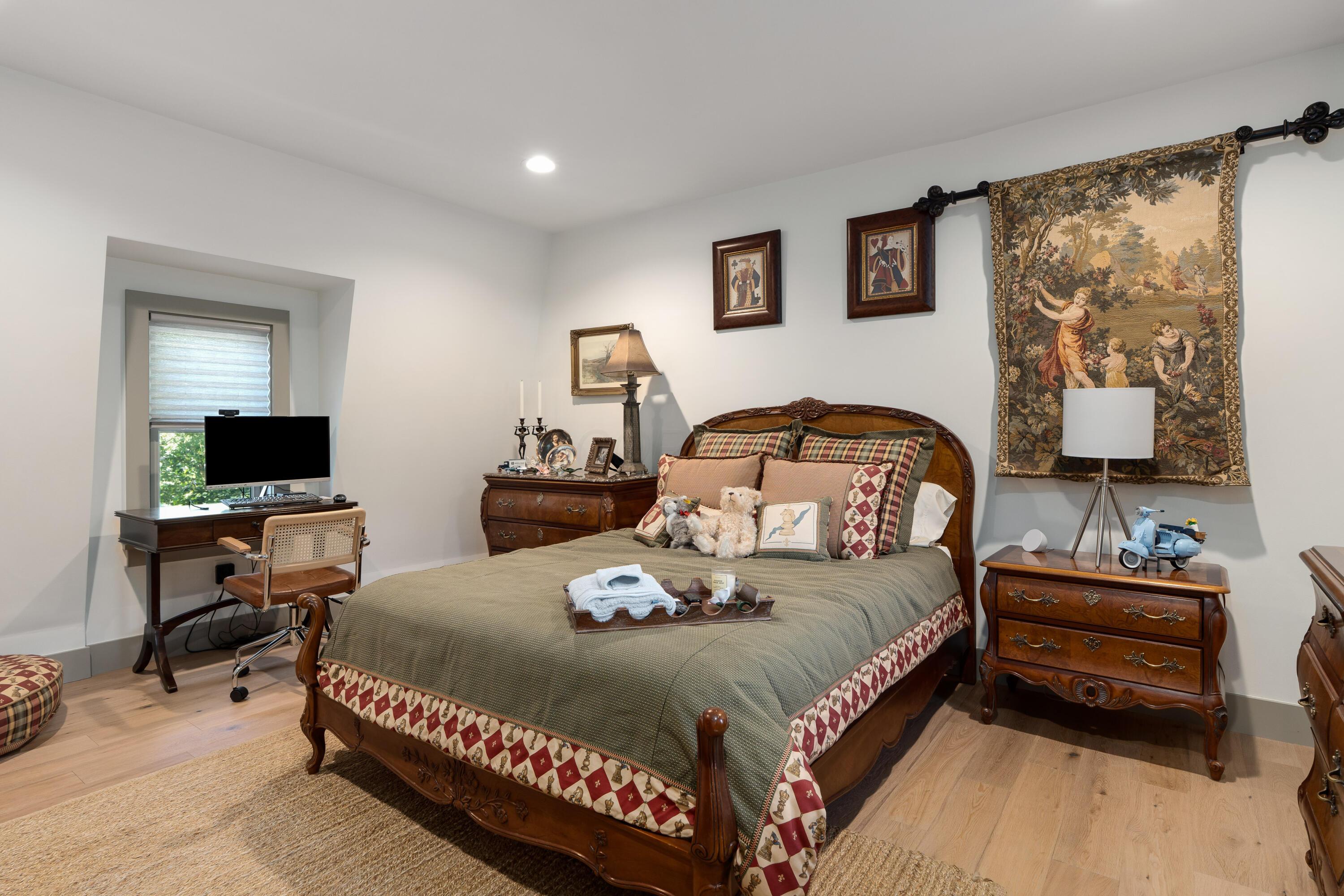 Furnished bedroom with an ornate wooden bed, antique-style dressers, a desk, and a tapestry.