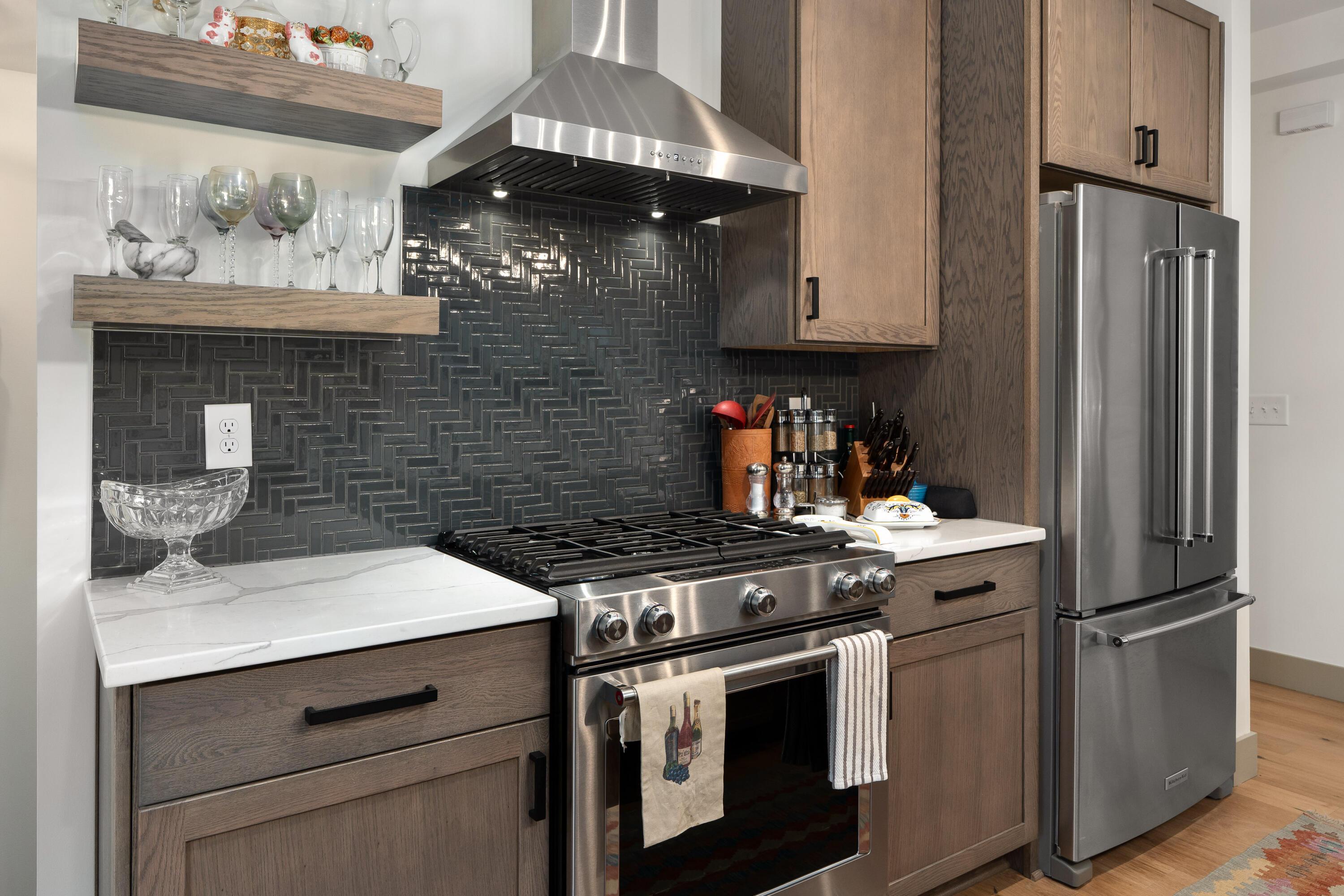 Modern kitchen with dark tile backsplash, wood cabinets, stainless steel range, and refrigerator.