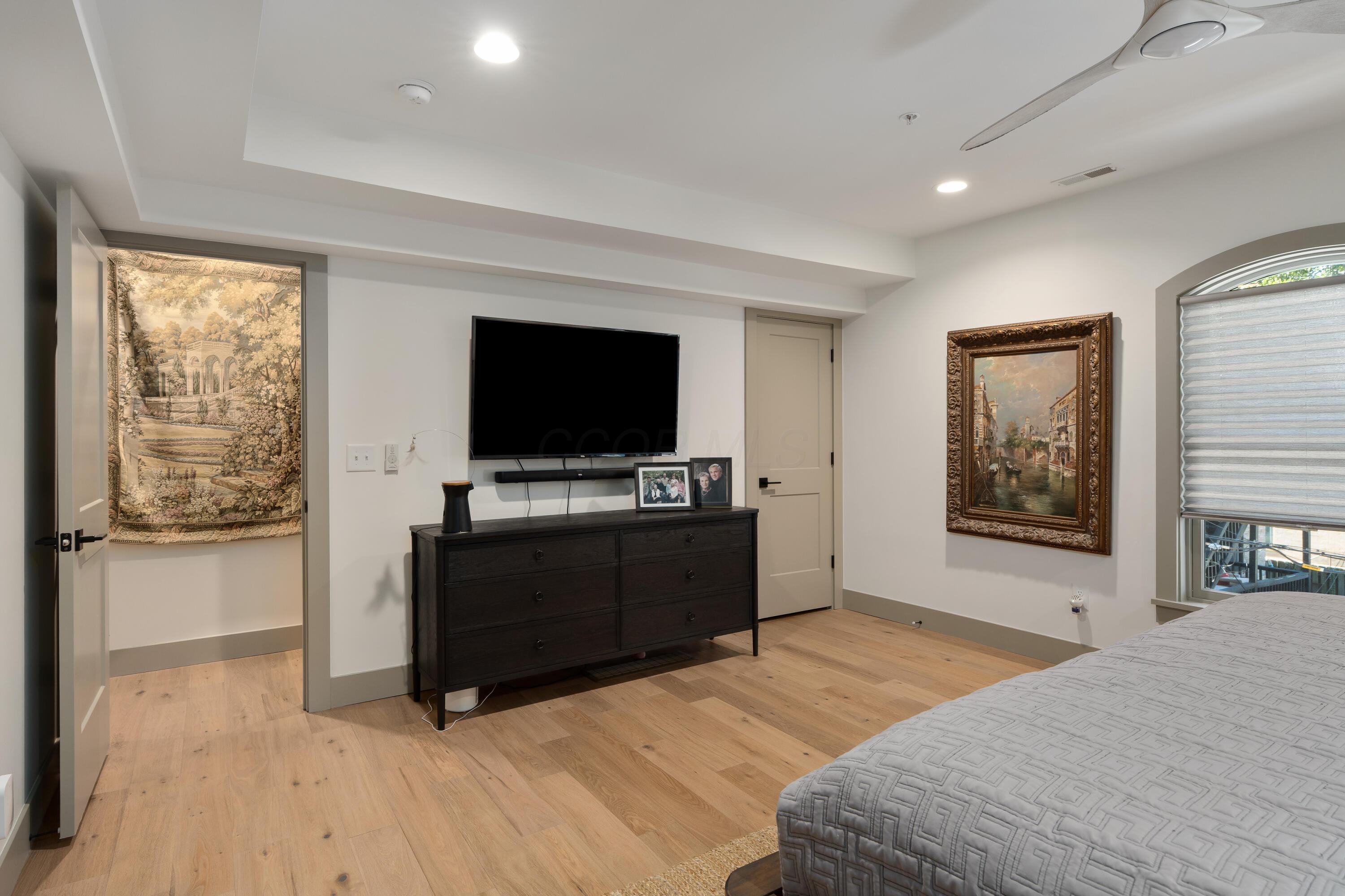 Bedroom with a gray bed, light oak floors, and a wall-mounted television above a dark dresser.