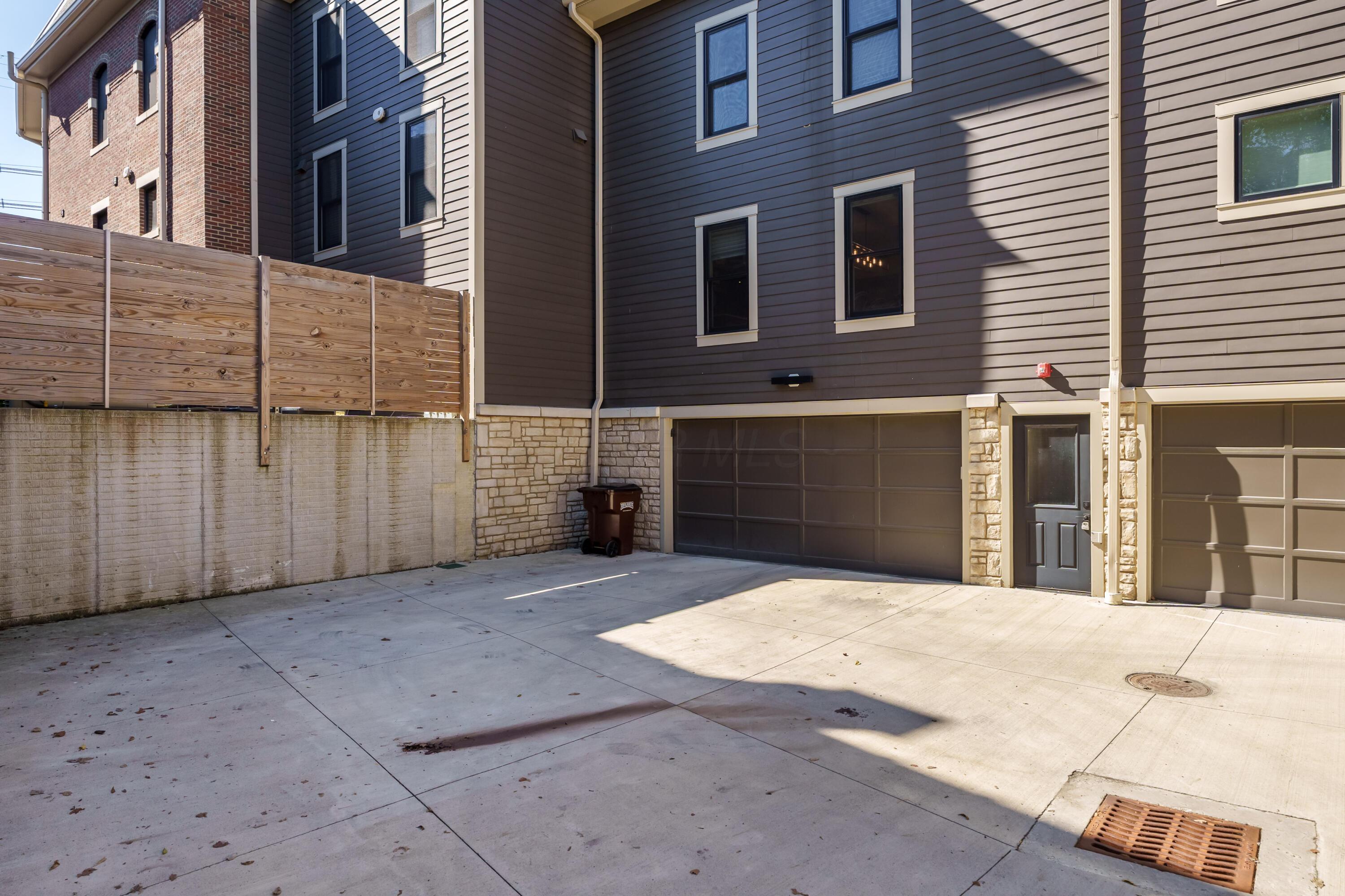 Townhouse rear with two garages, concrete driveway, and wooden privacy fence.