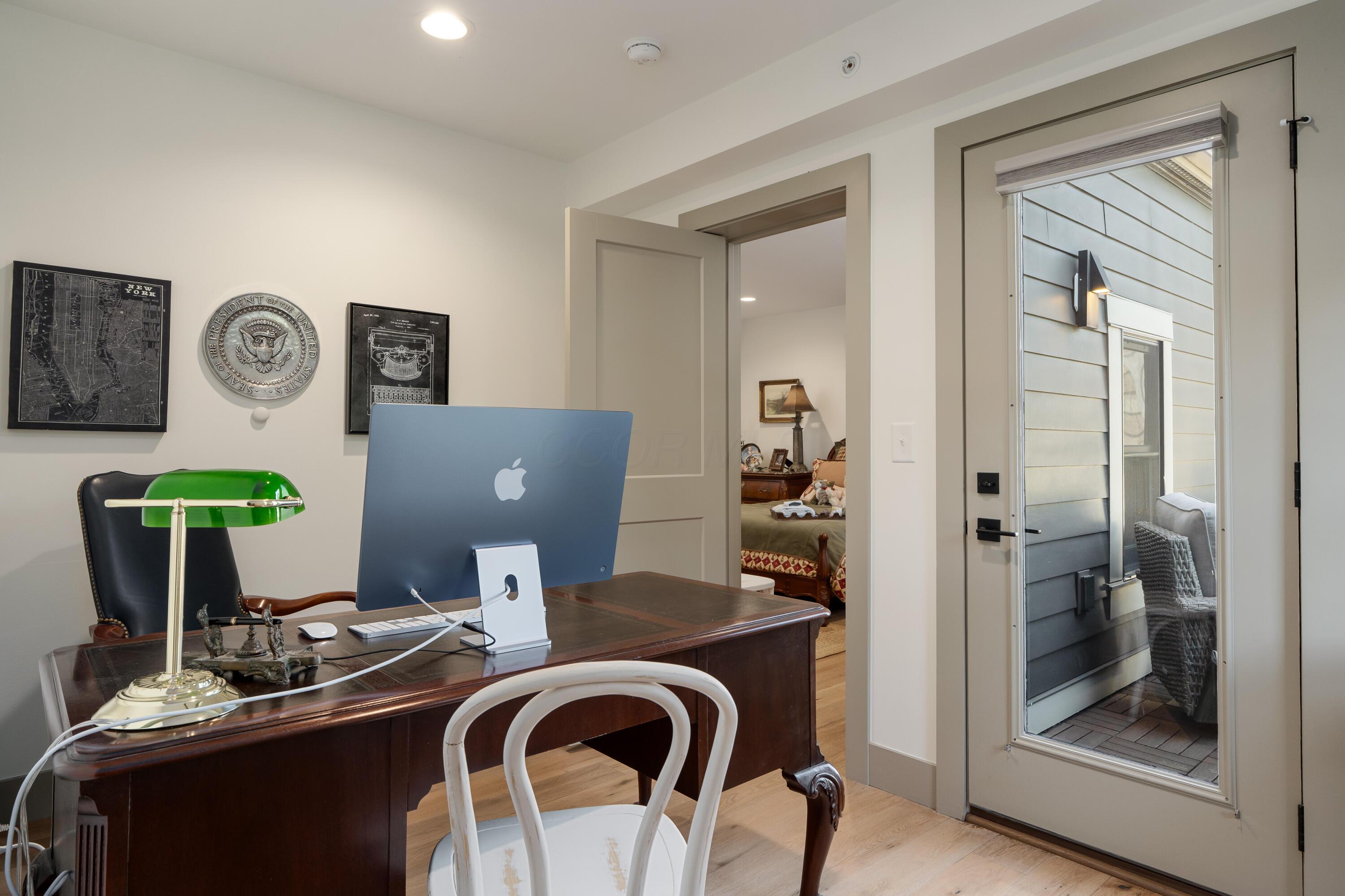Furnished home office with a dark wood desk and glass door opening onto a patio.