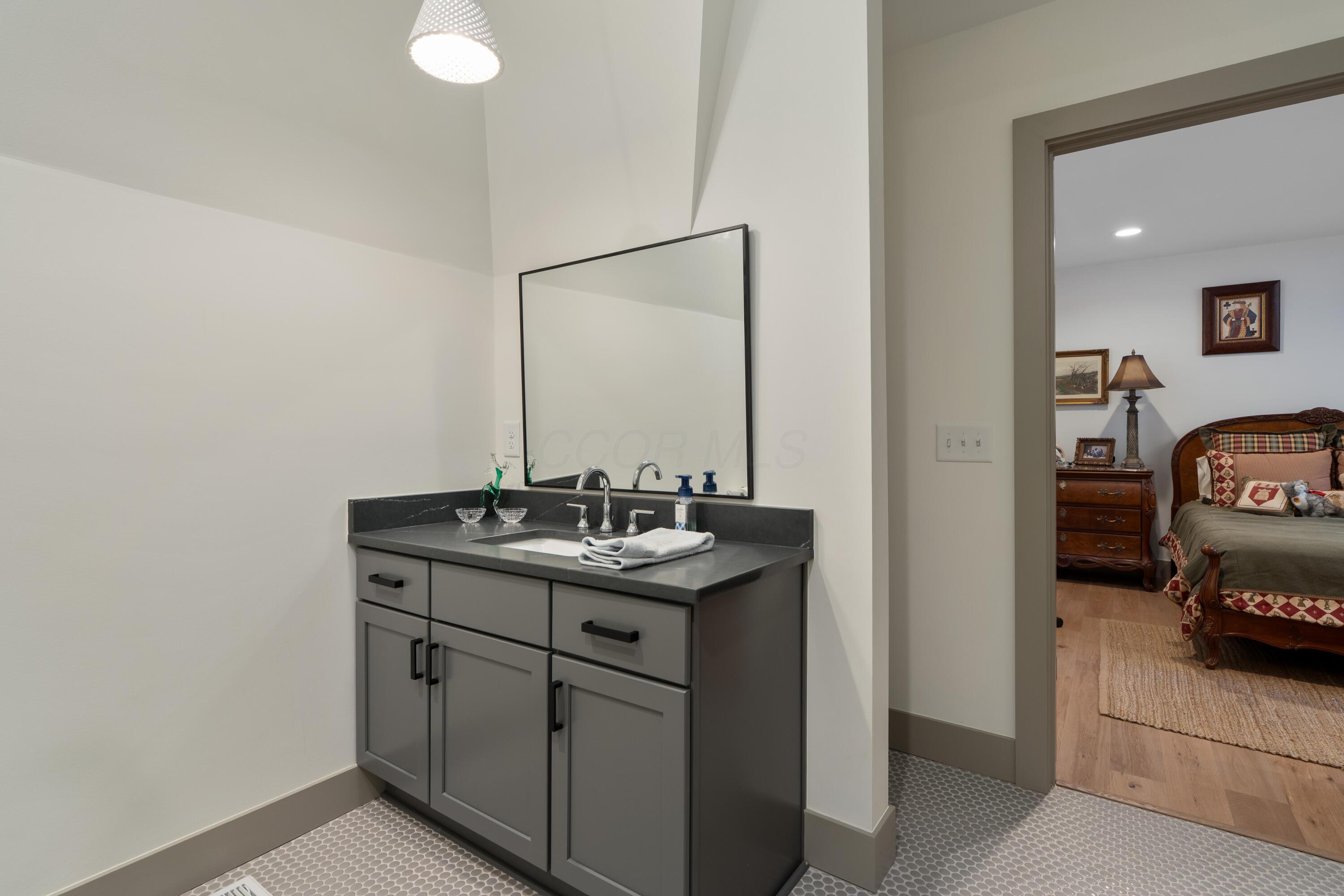 Bathroom vanity with dark gray cabinetry and a large mirror, opening onto a furnished bedroom.