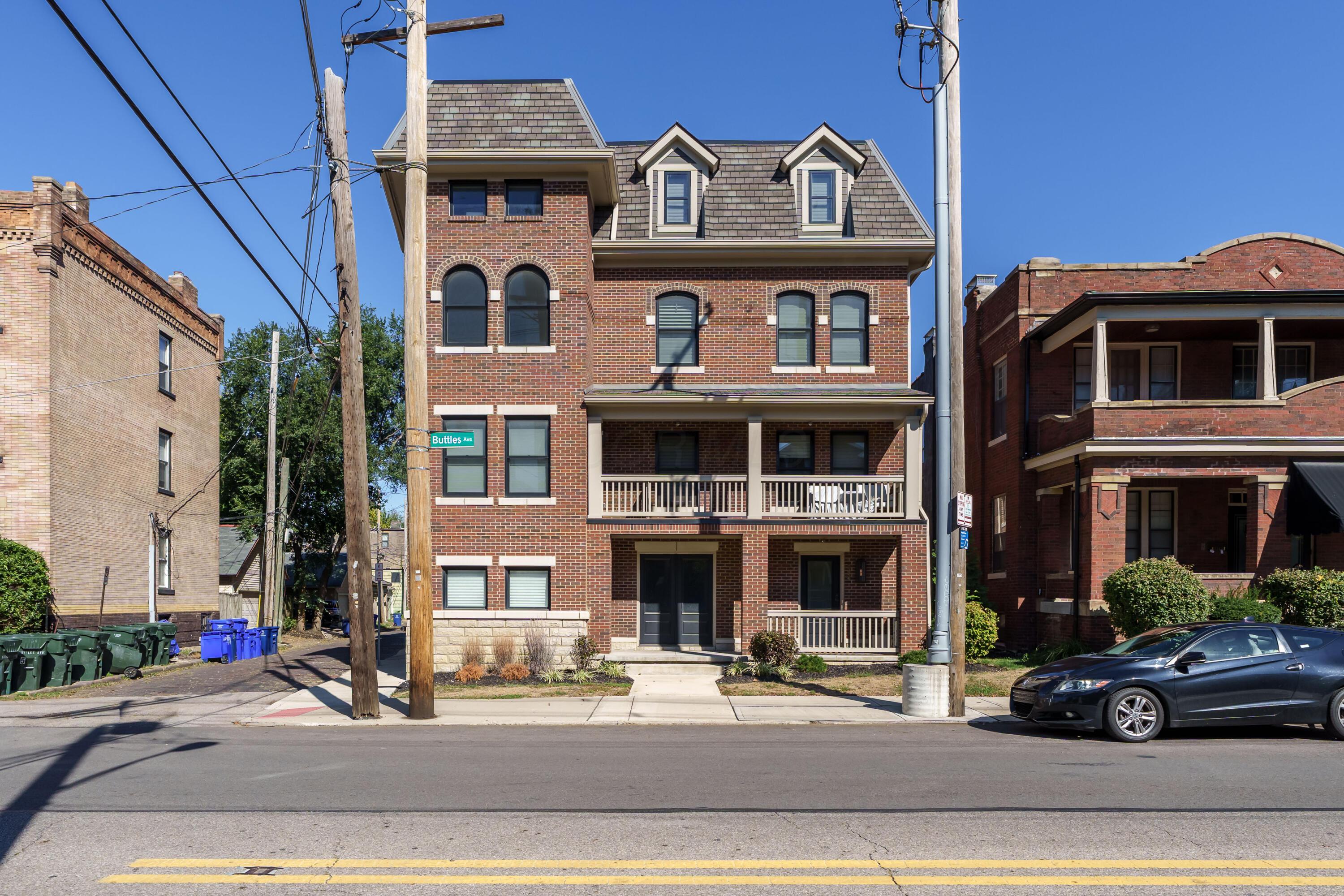 Multi-story red-brick residence with dormers and stacked porches on a sunny urban street.