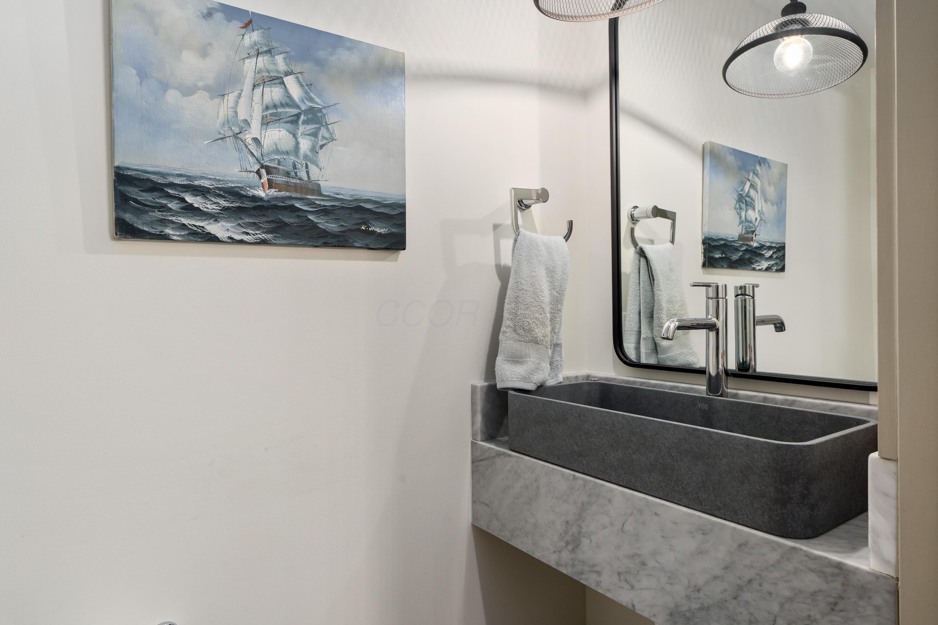 Bathroom vanity with a dark vessel sink, chrome faucet, marble counter, and sailing ship painting.