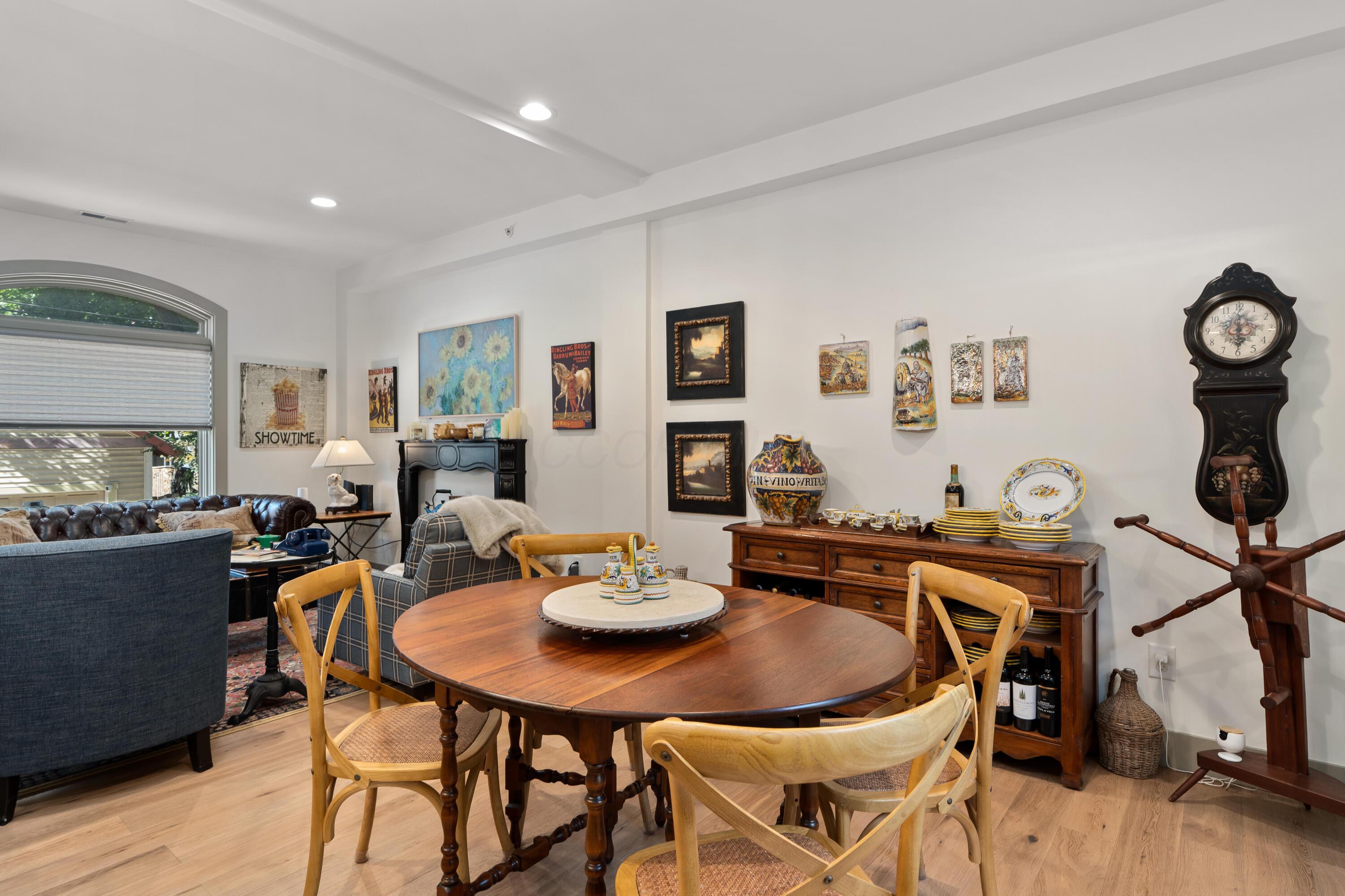 Dining and living area with a round wooden table, ceramic displays, antique clock, and arched window.
