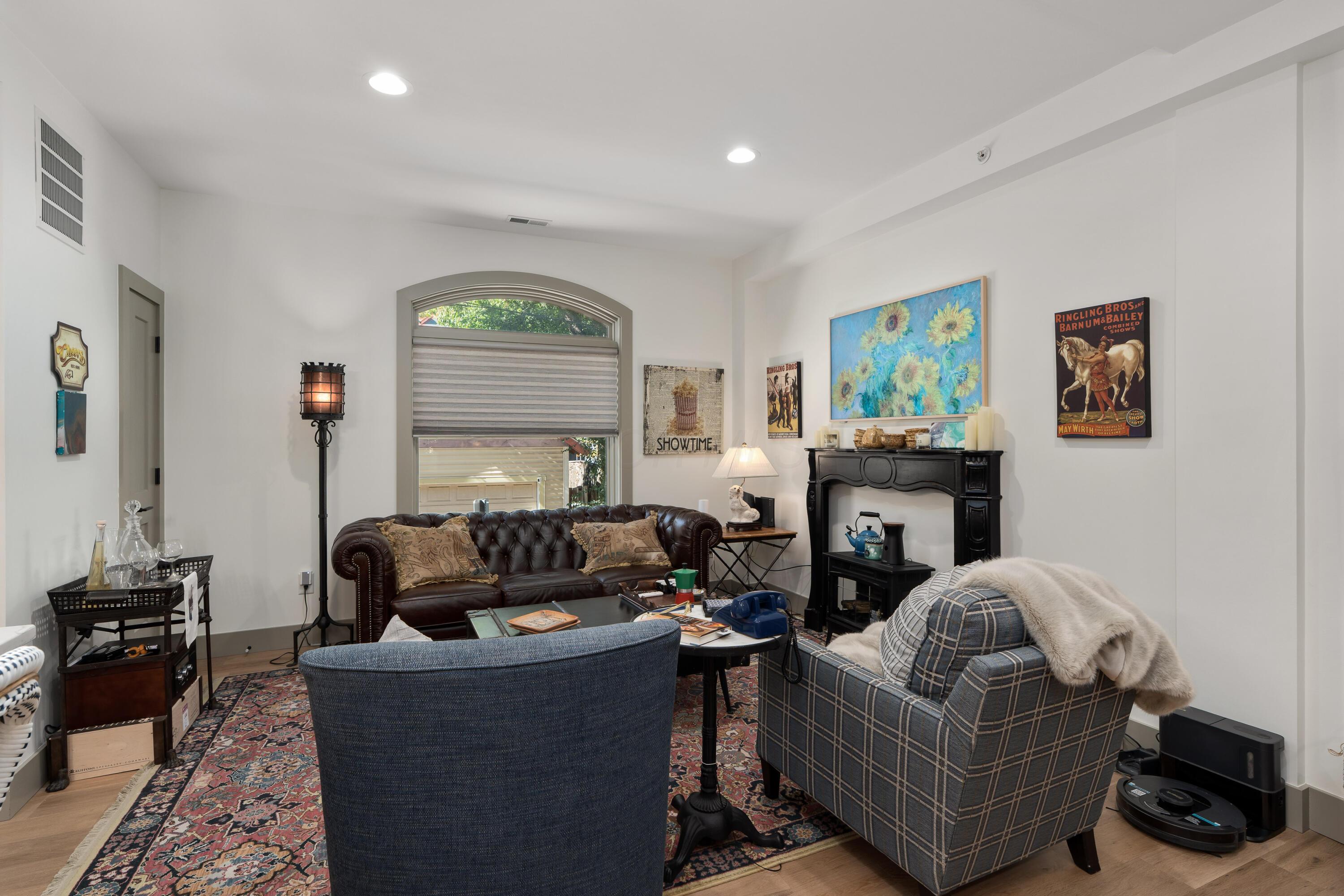 Furnished living room with a leather sofa, plaid armchair, patterned rug, and arched window.
