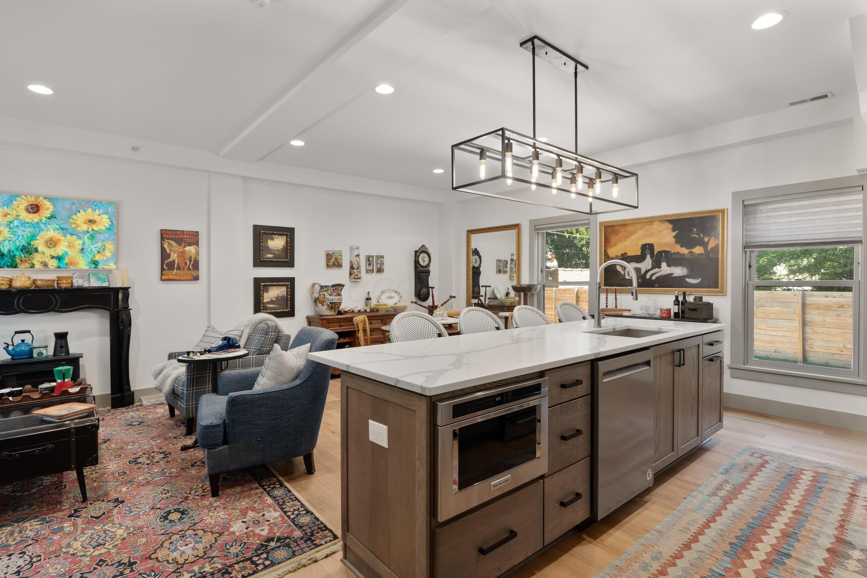 Open-plan kitchen with a large veined-stone island, wood cabinetry, and a rectangular pendant light.
