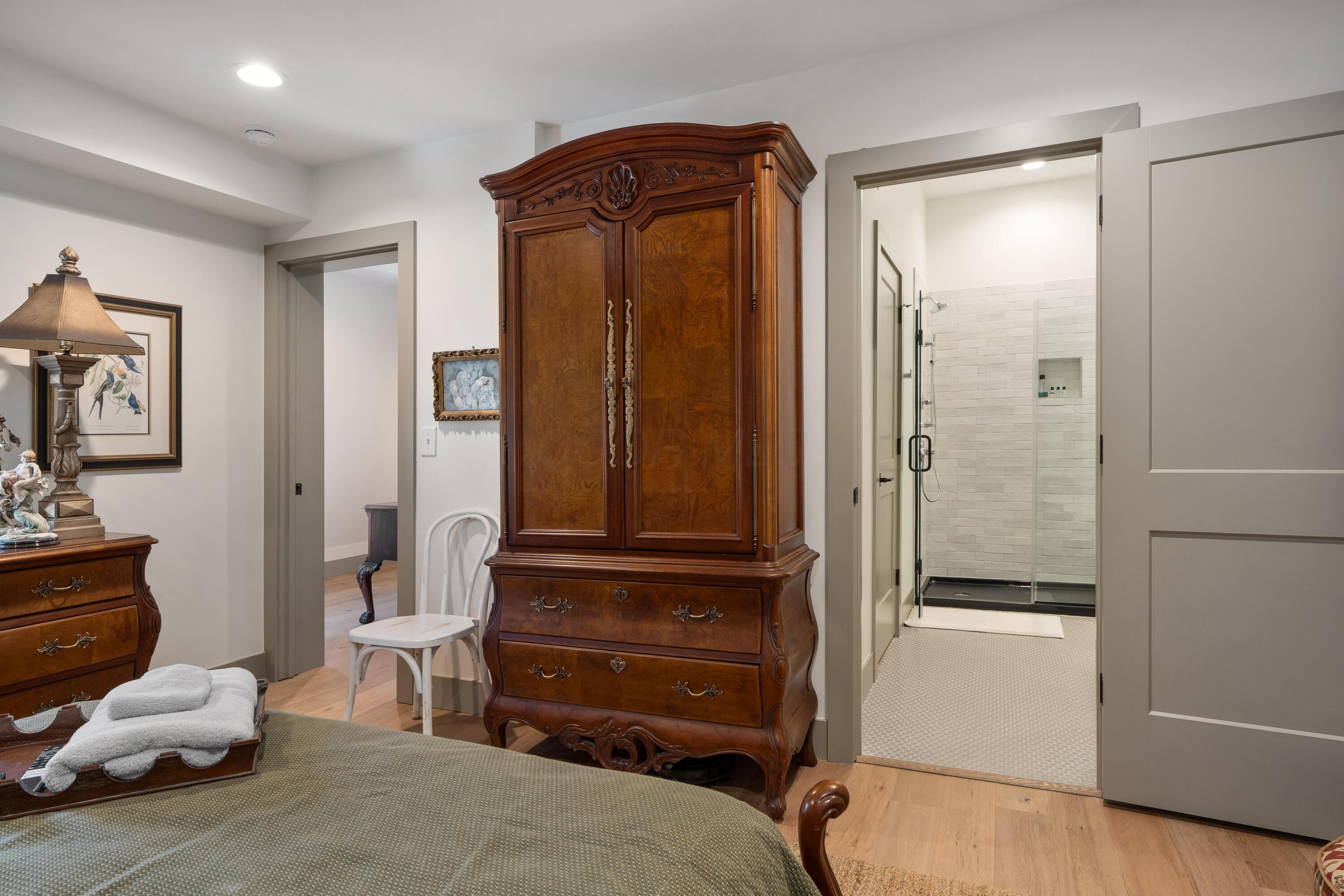 Bedroom with an ornate wood armoire and an open doorway to a tiled walk-in shower.