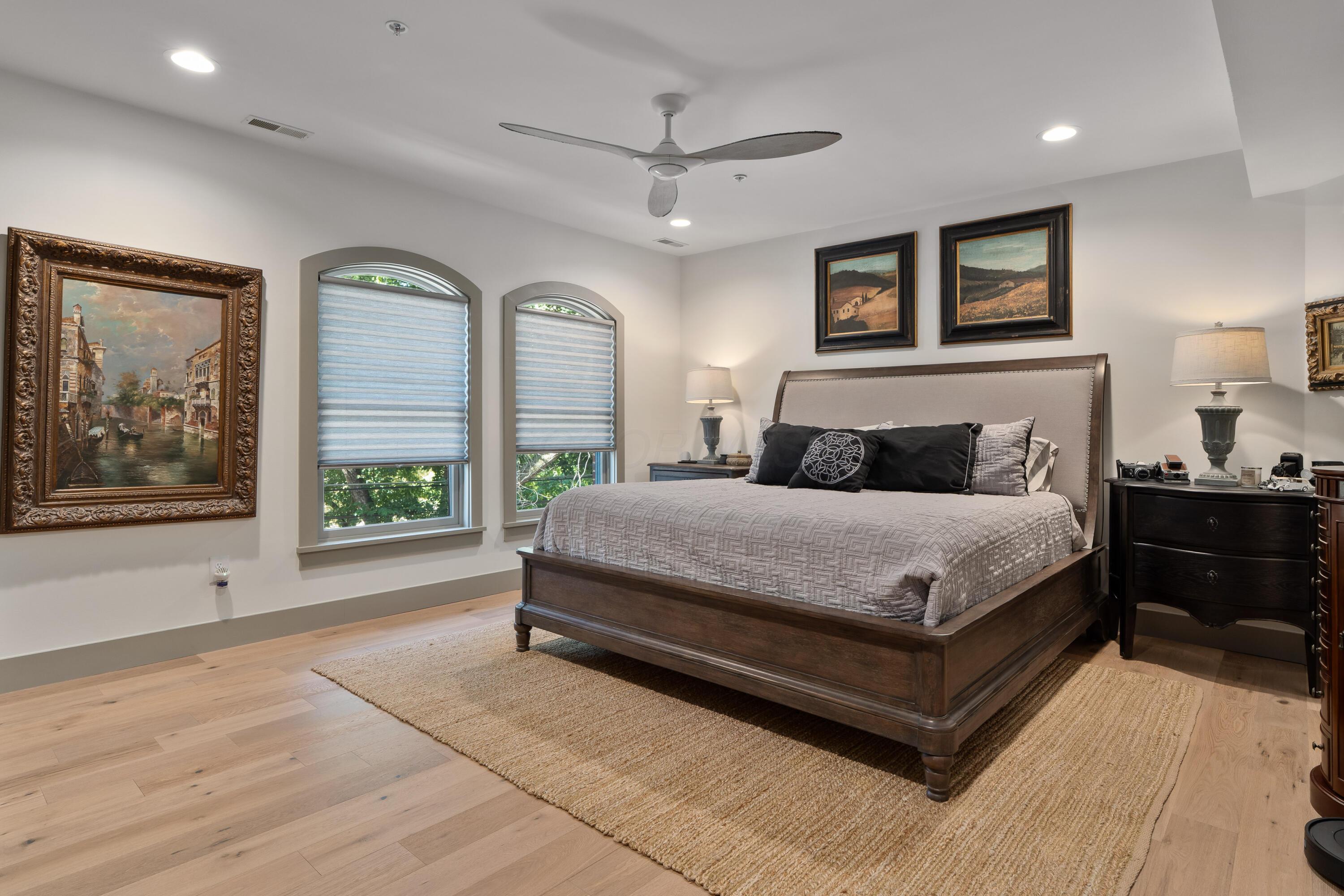 Bedroom with a dark wood bed, black accent pillows, and two arched windows with striped shades.