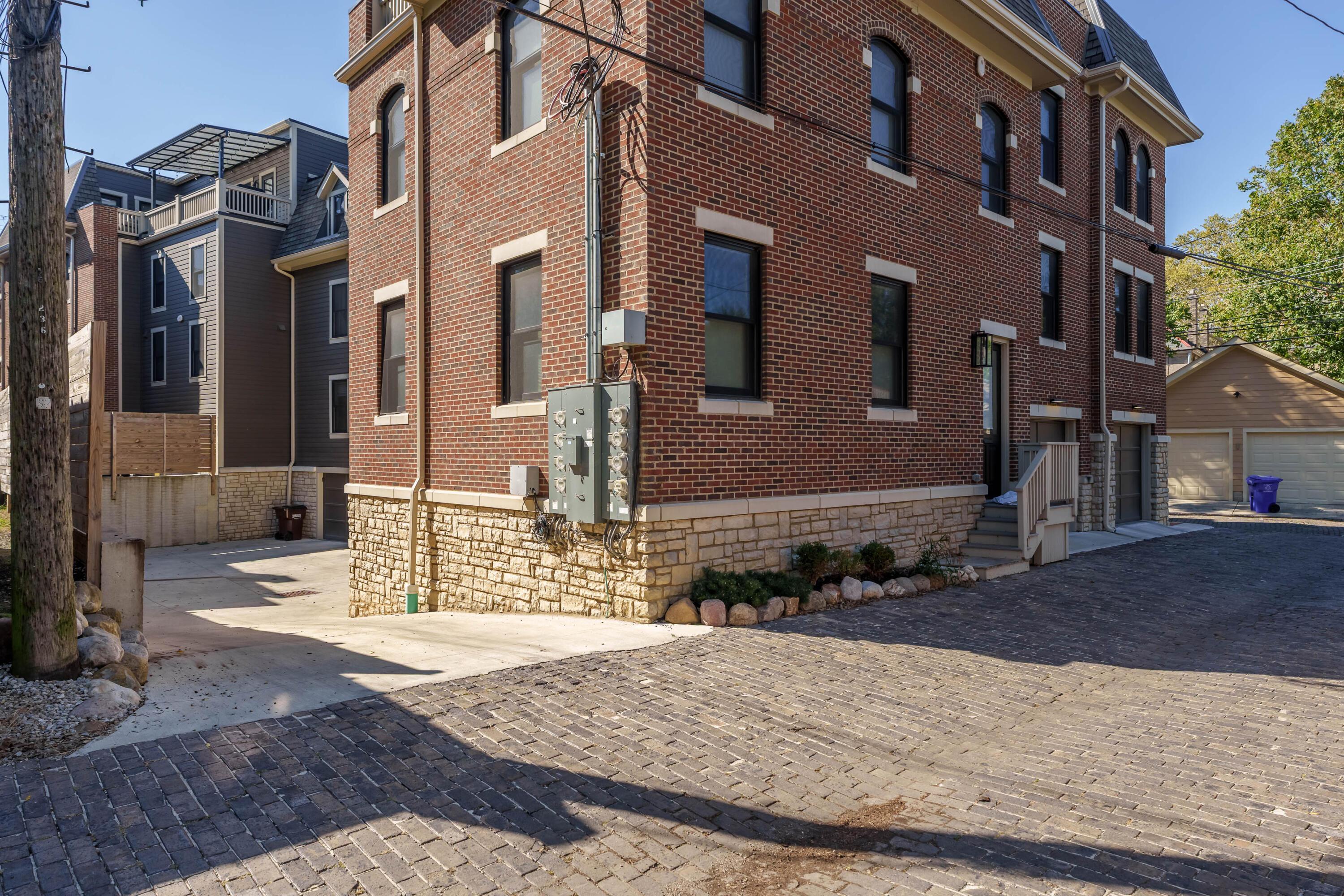 Red brick multi-story property with stone foundation and a side entrance beside a brick-paved driveway.