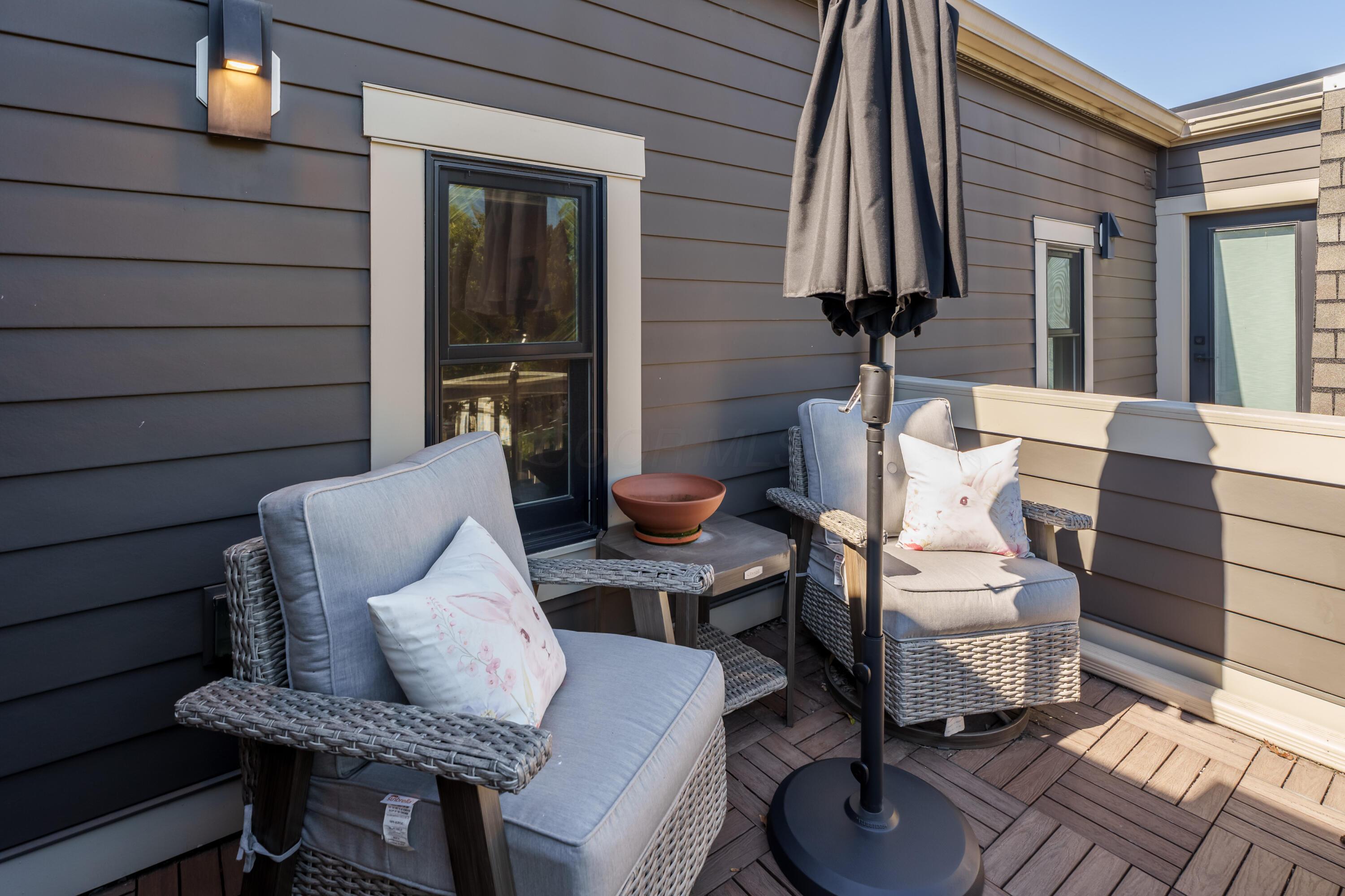 Rooftop patio with cushioned wicker chairs, a closed umbrella and dark wood decking.