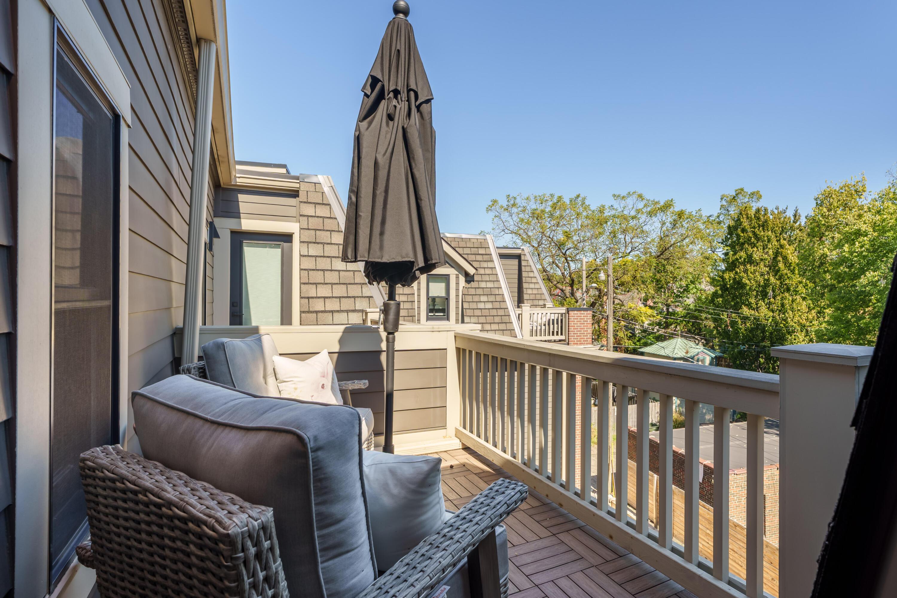 Furnished deck with cushioned seating, a closed umbrella, and views over nearby rooftops.