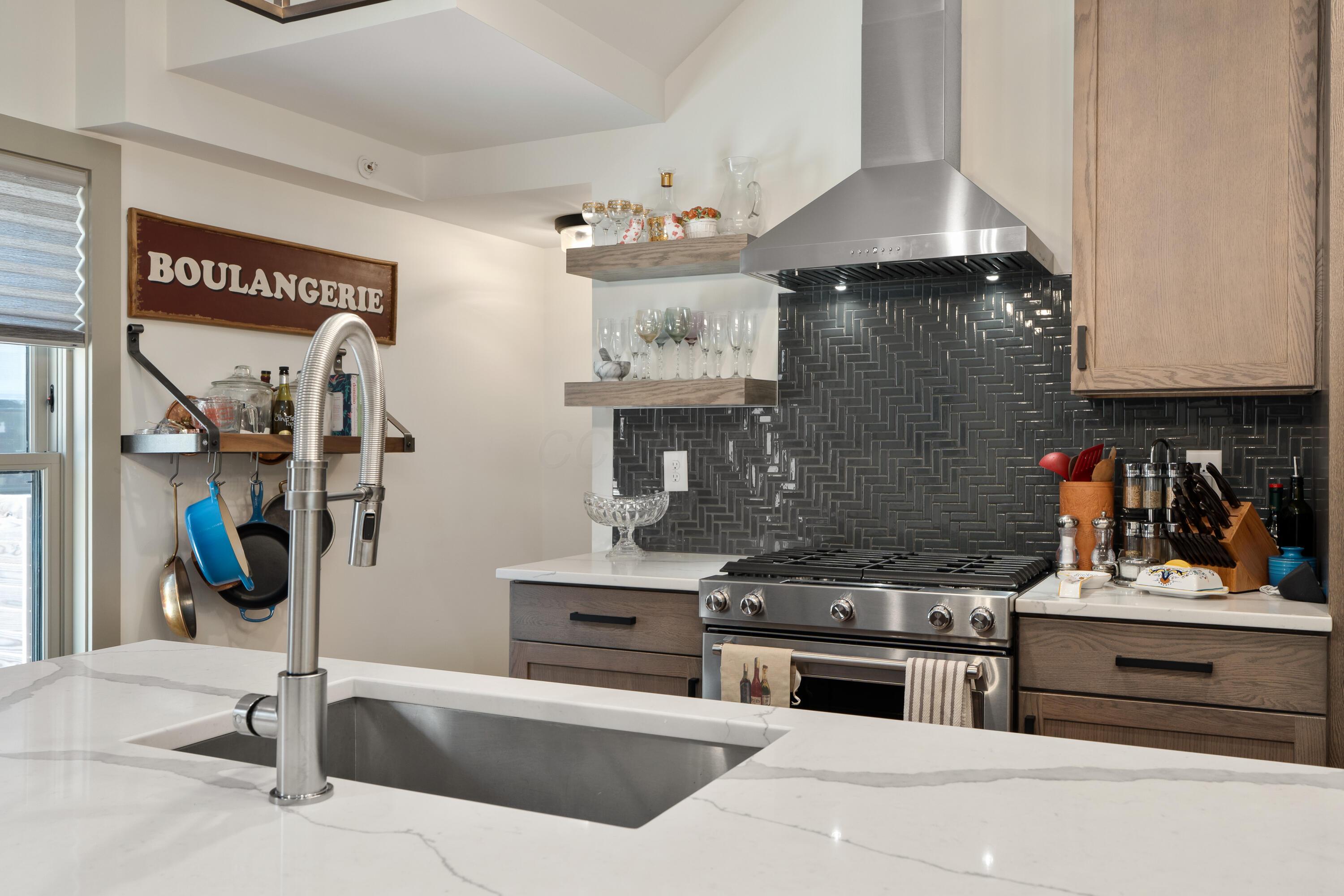 Kitchen with a deep sink, stainless steel range, dark tile backsplash, and hanging cookware.