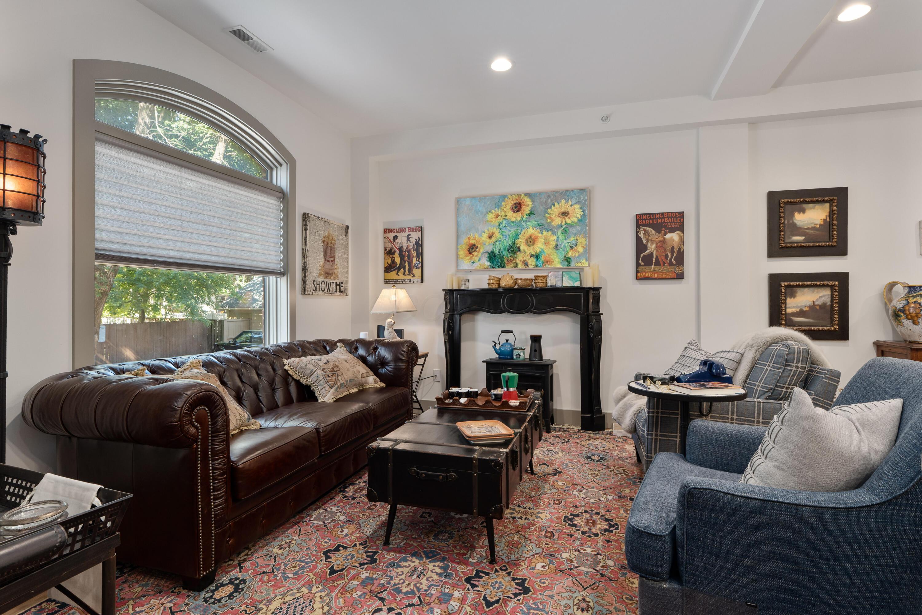 Furnished living room with an arched window, dark leather sofa, blue armchairs, and patterned rug.