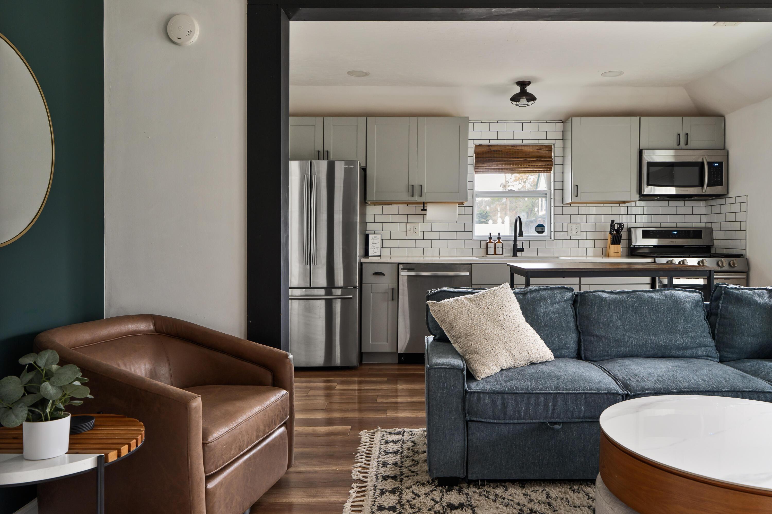 Open-plan living room and kitchen with white subway tile, stainless appliances, and a blue sofa.